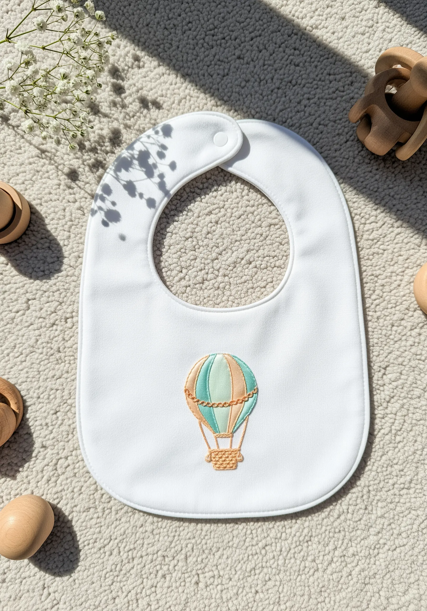 A white baby bib with a soft pastel hot air balloon embroidered in the center.