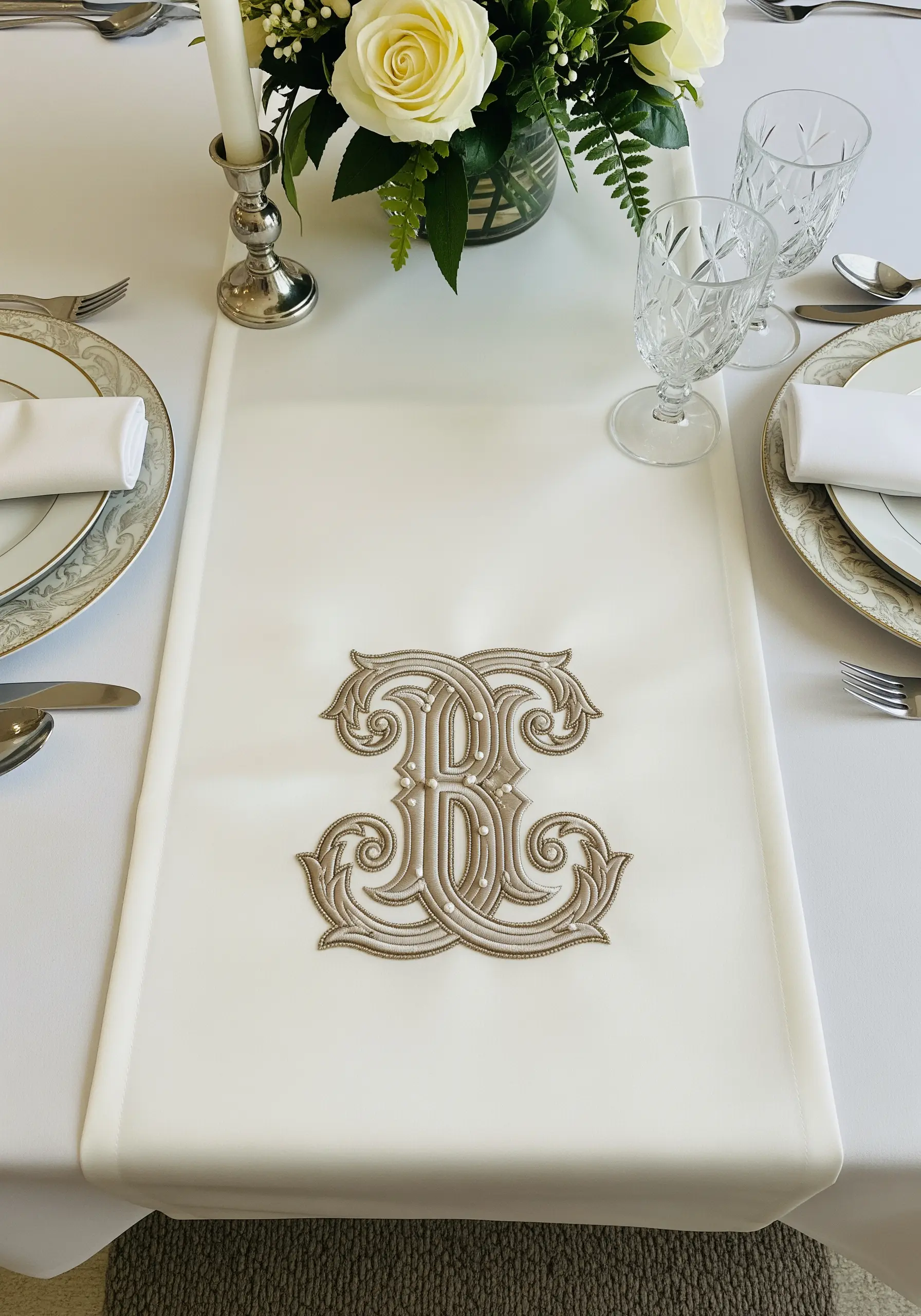 A highly ornate, three-dimensional monogram embroidered in taupe on a white table runner.