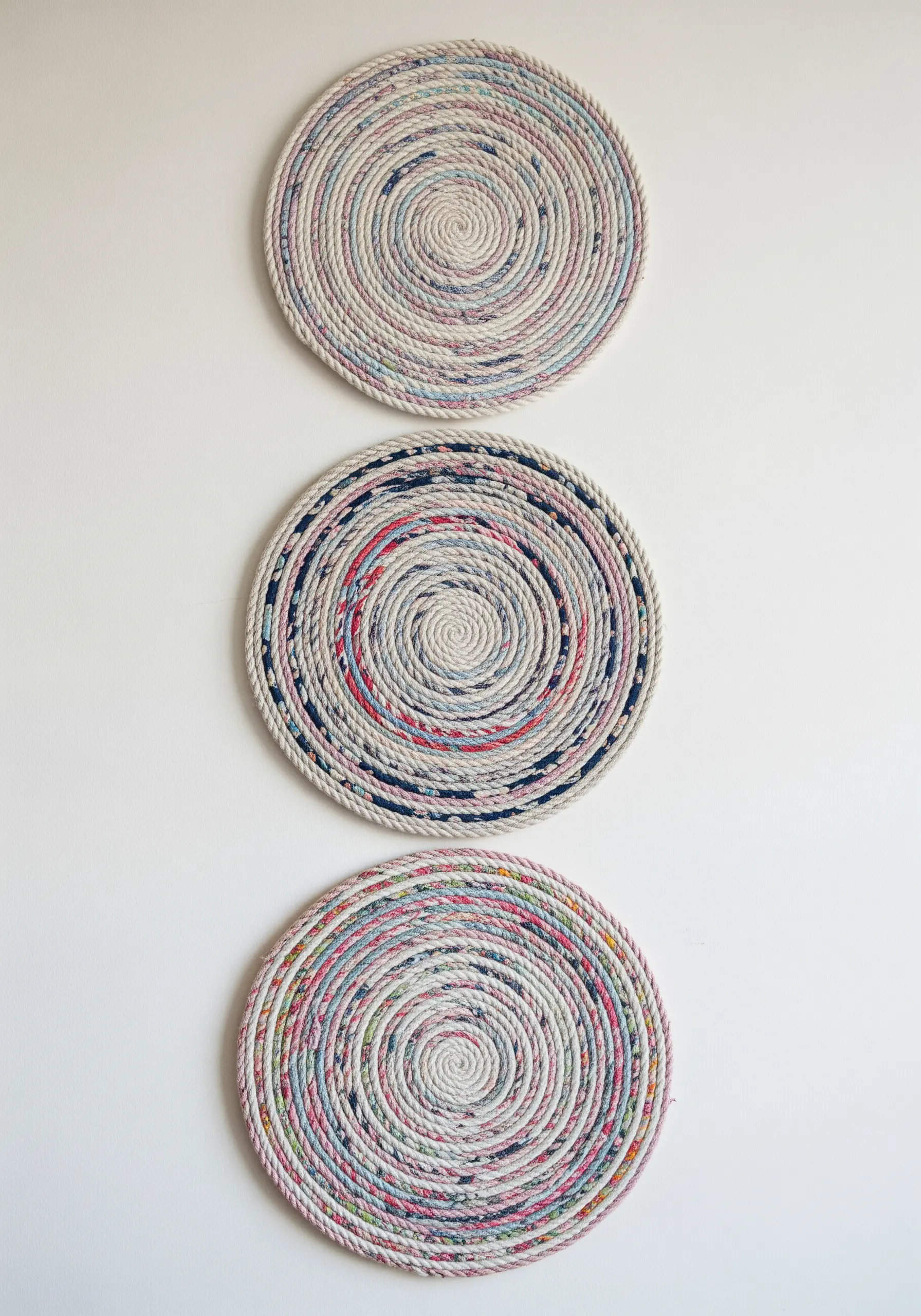 Three circular wall hangings made from fabric-wrapped rope coiled into flat spirals.