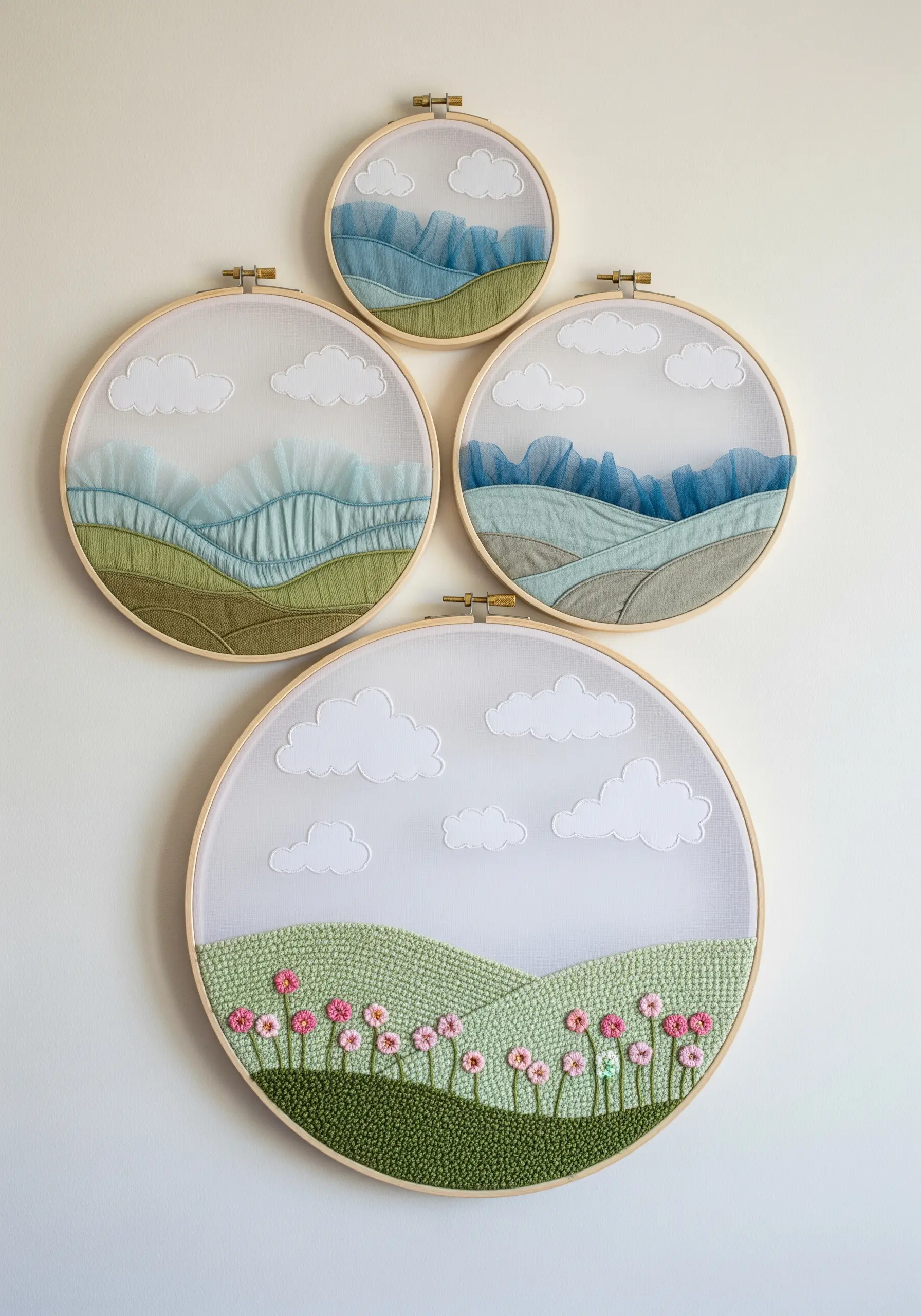 A set of four embroidery hoops showing layered landscapes with punch needle hills and tulle mountains.