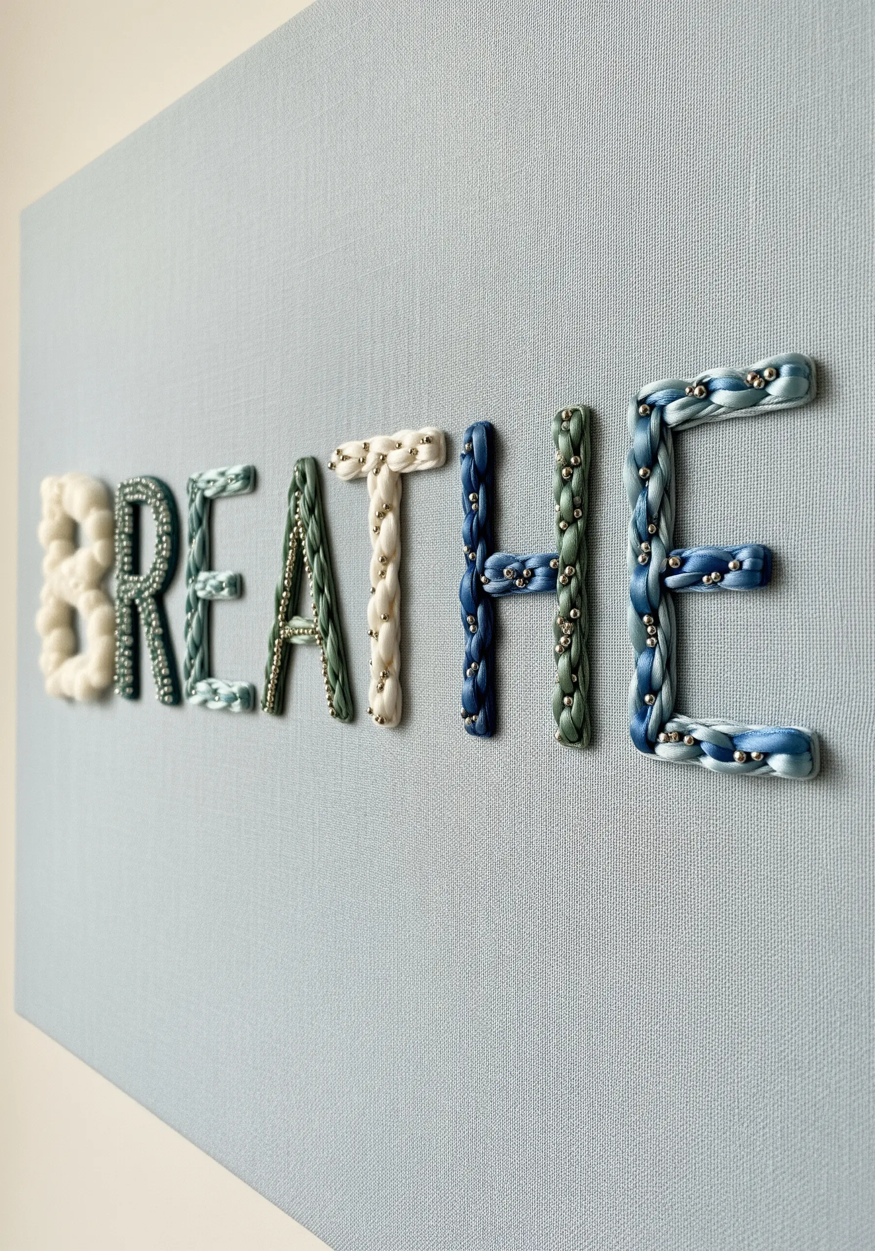 The word BREATHE embroidered with braided, beaded floss in shades of blue.