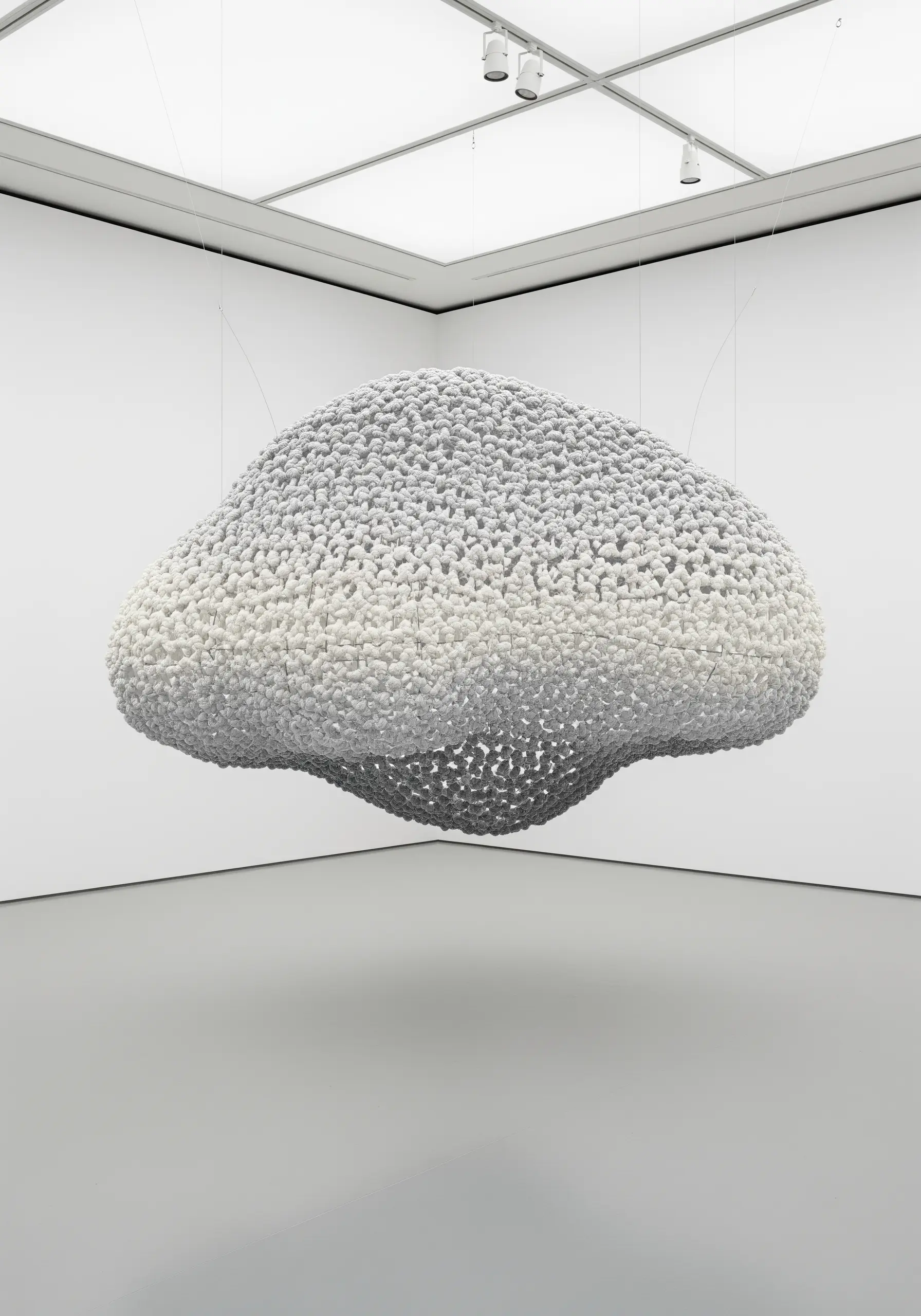A large, floating cloud sculpture made entirely of tightly packed white and grey knots.