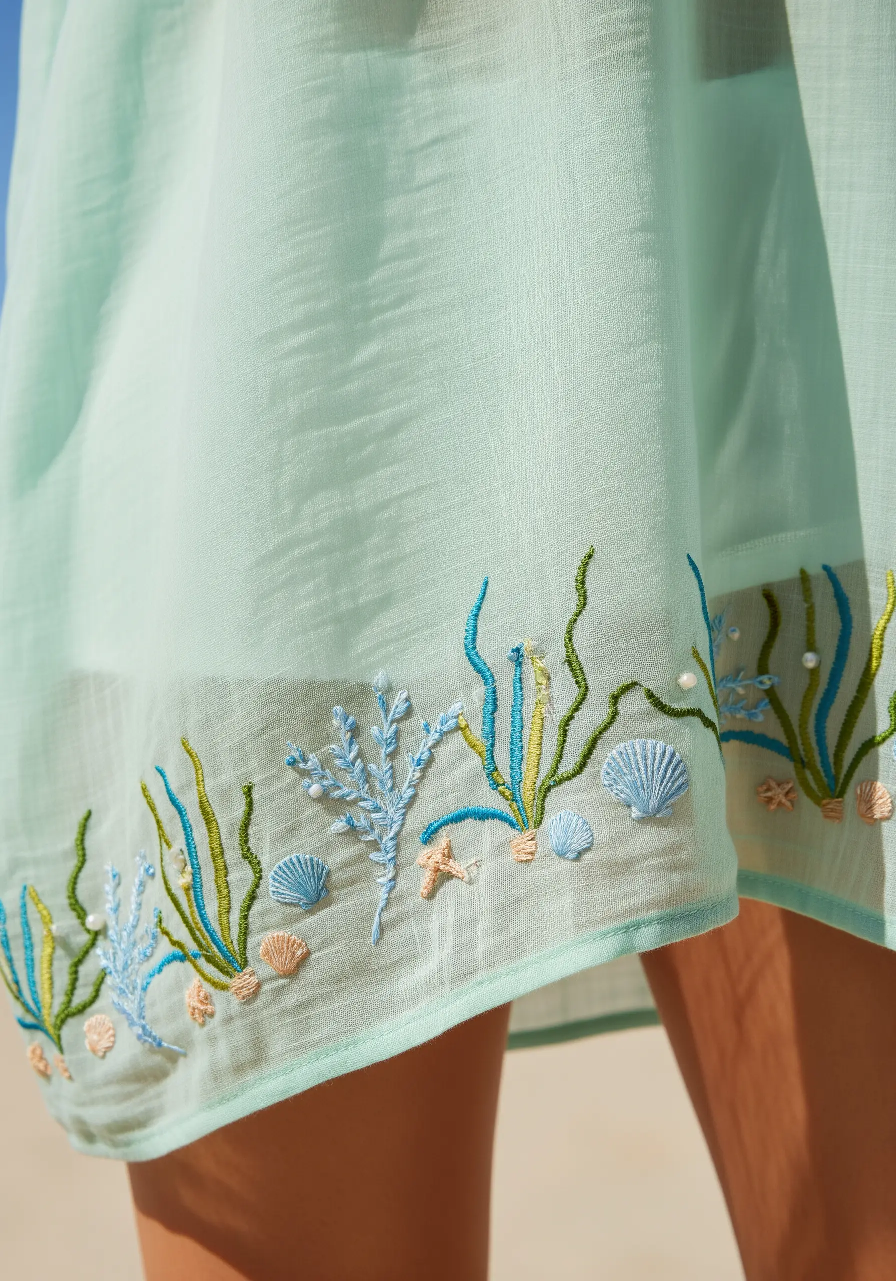 Whimsical underwater-themed embroidery with coral and shells on a light green hem