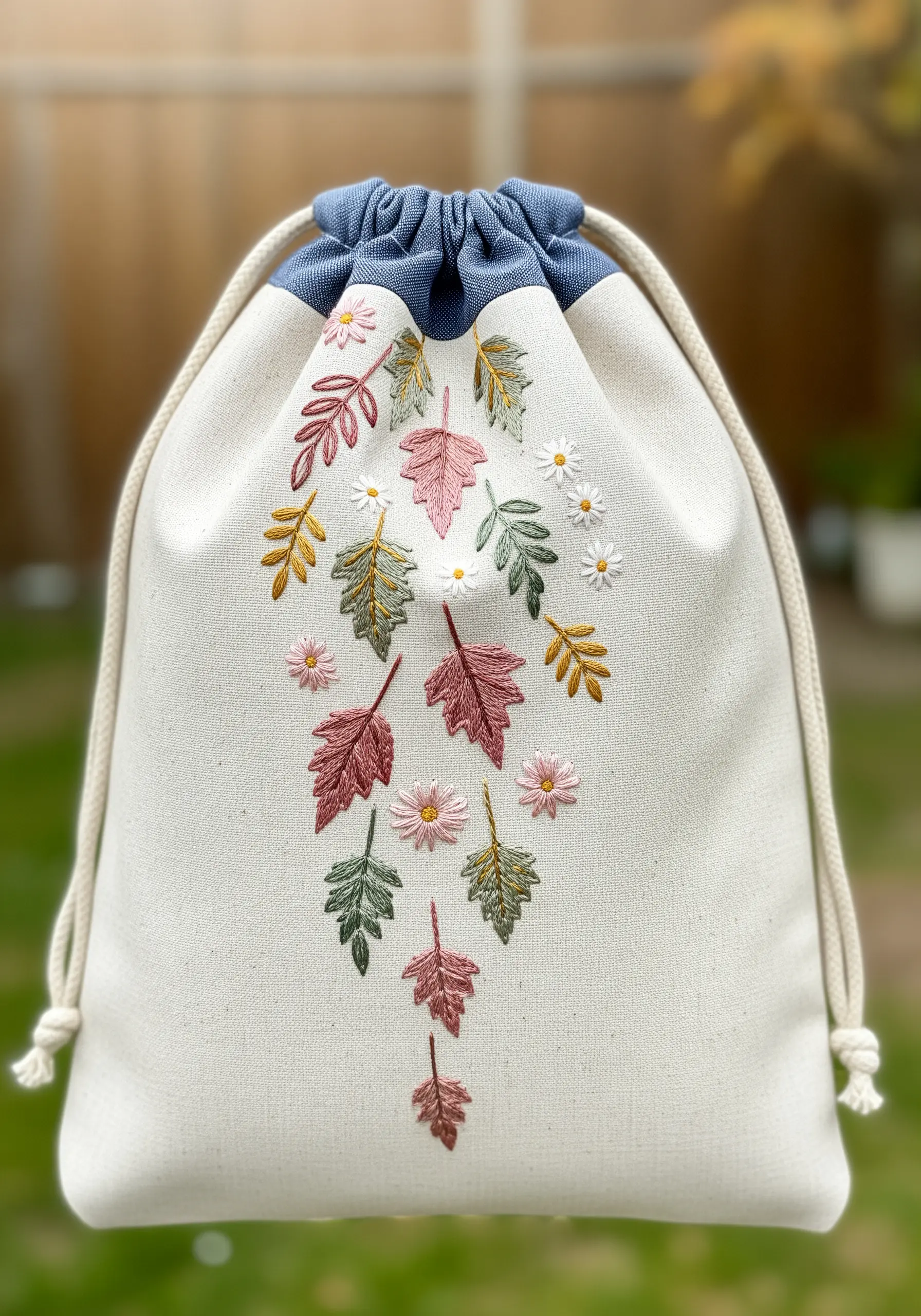 A cascade of embroidered leaves in pink, gold, and green falling down a drawstring bag.