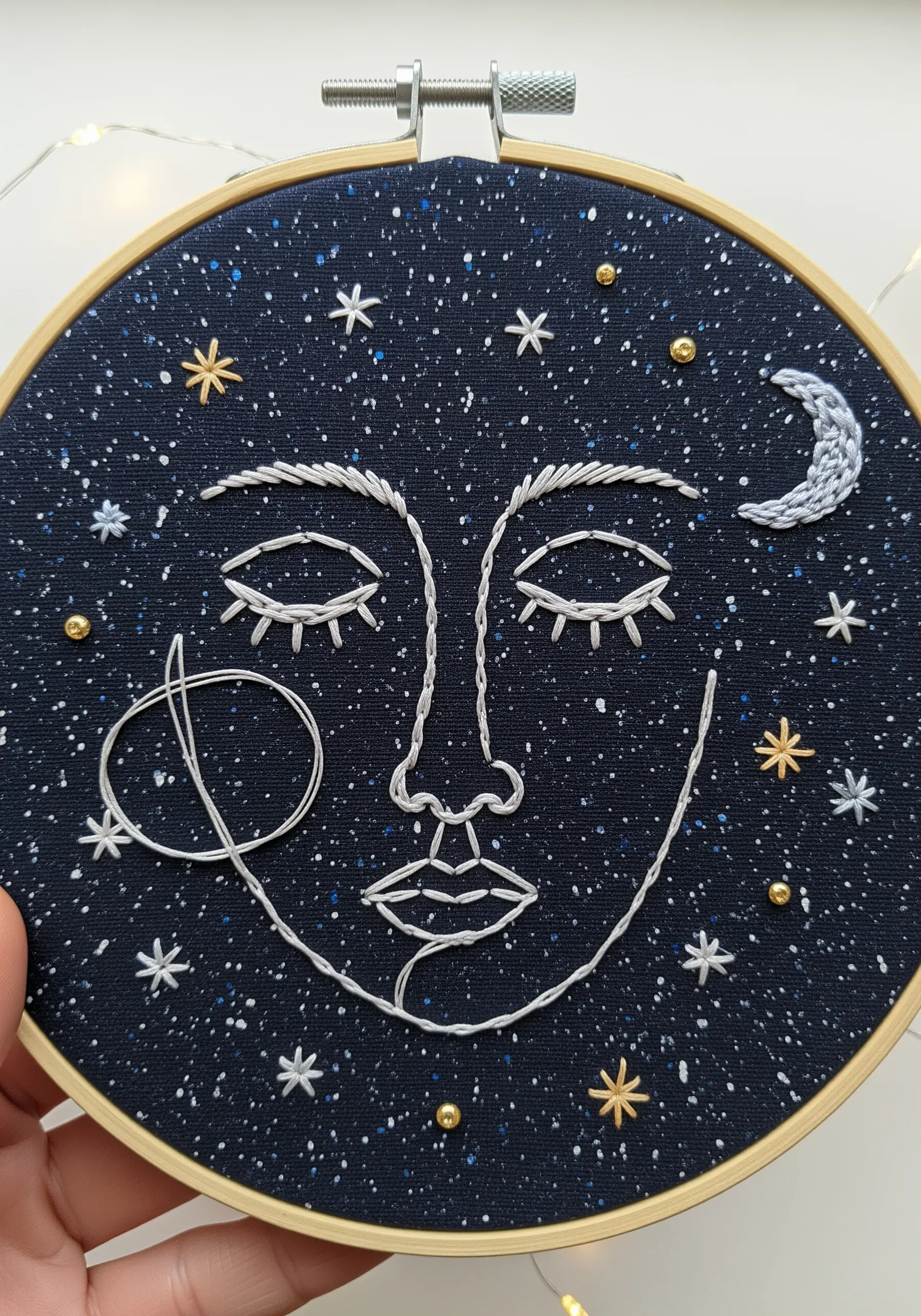 A celestial face on dark fabric, embellished with stars, beads, and a crescent moon.