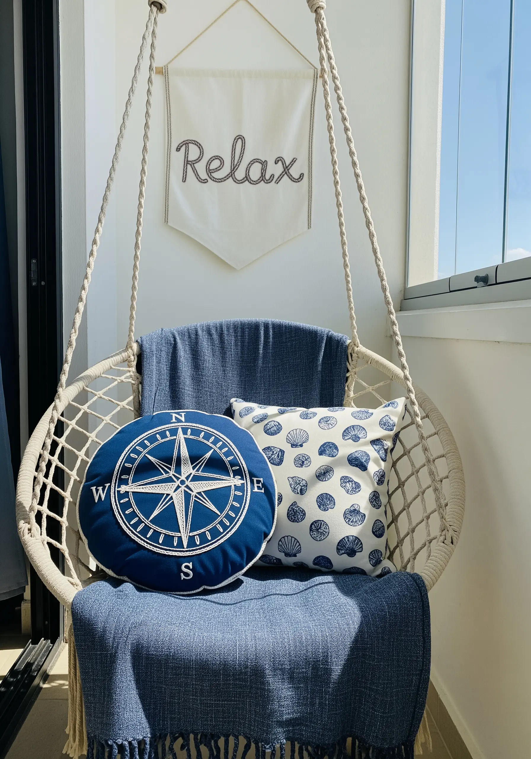 Balcony chair with pillows embroidered with a compass rose and seashells, plus a 'Relax' banner.