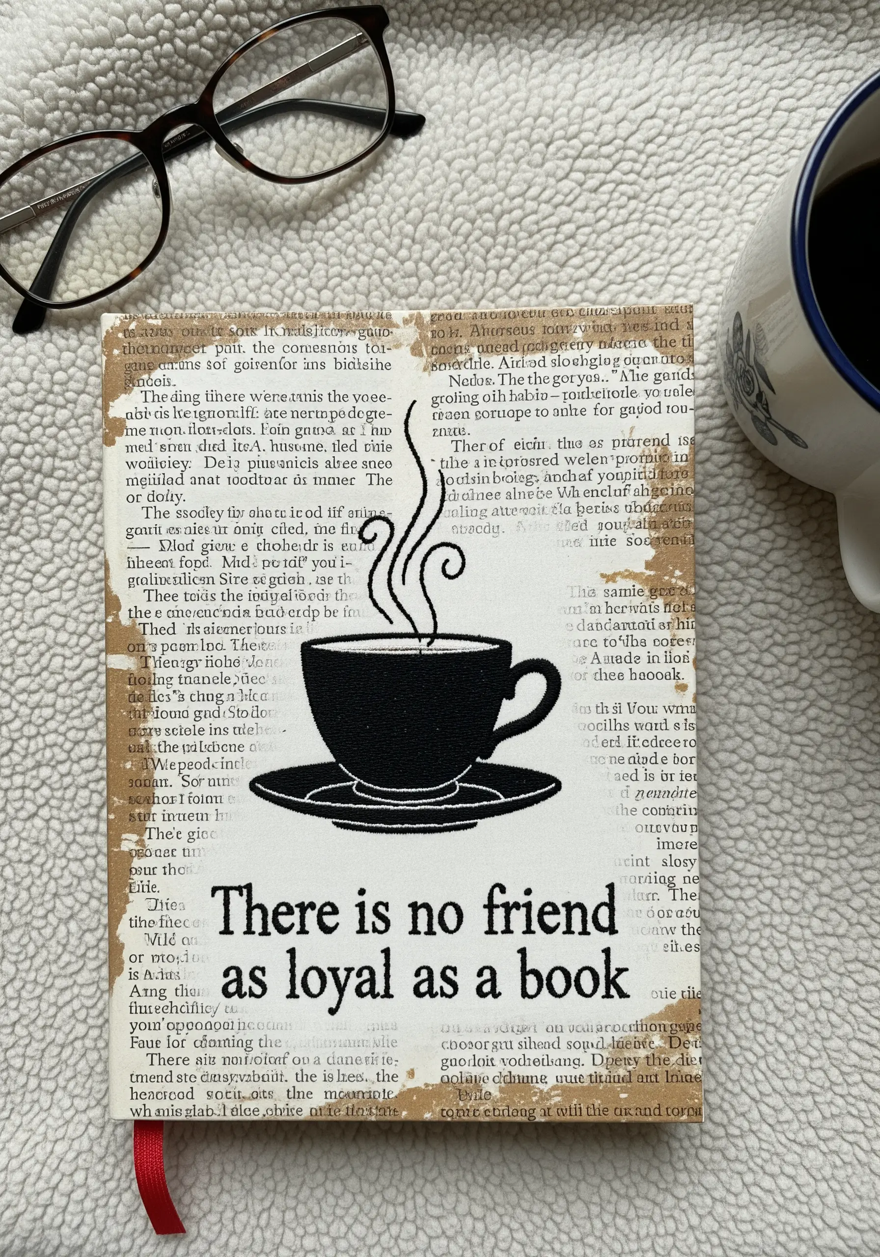 A black fabric appliqué of a coffee cup stitched onto a collage of old book pages.