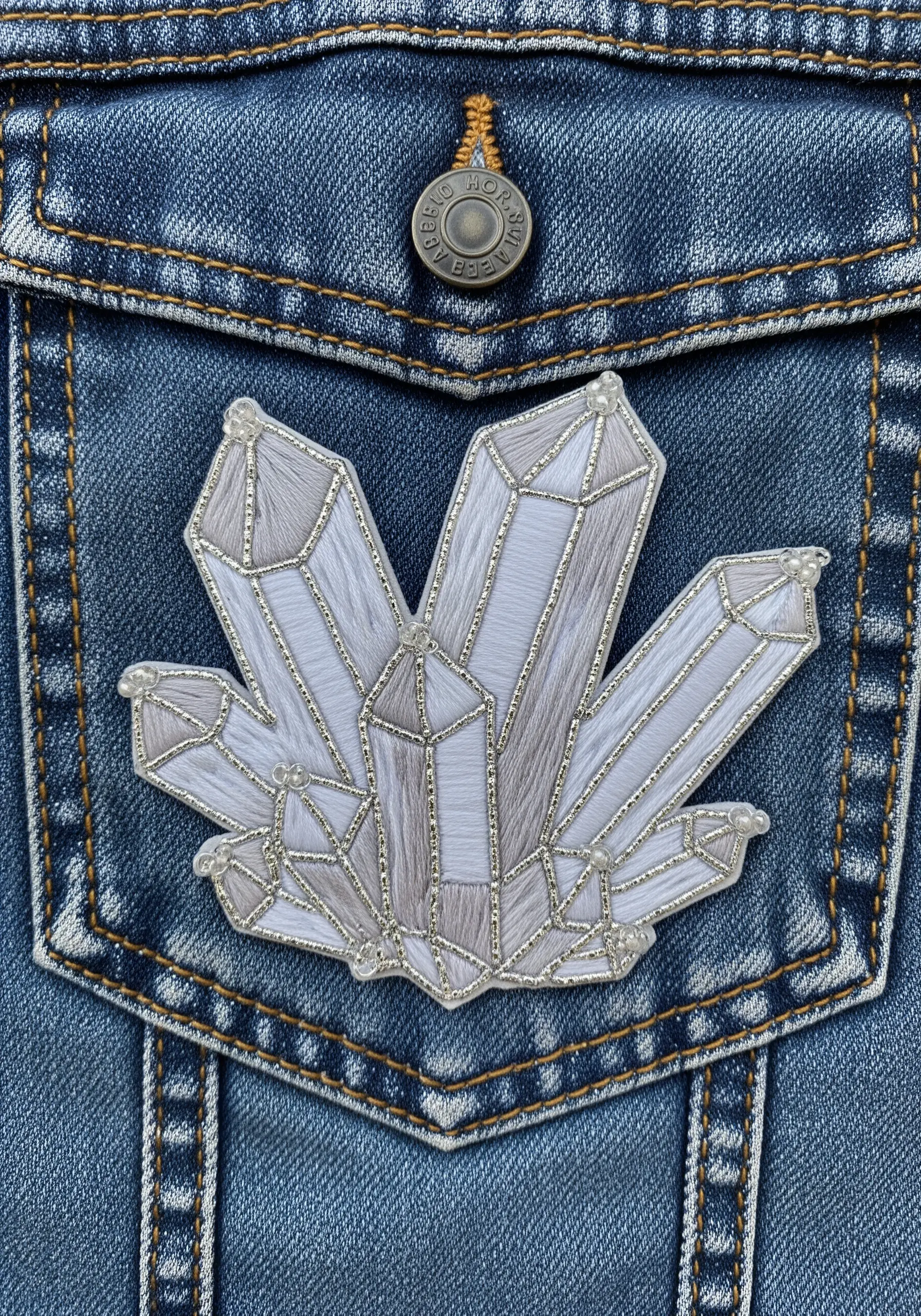 An embroidered patch of a crystal cluster on a denim jacket pocket.