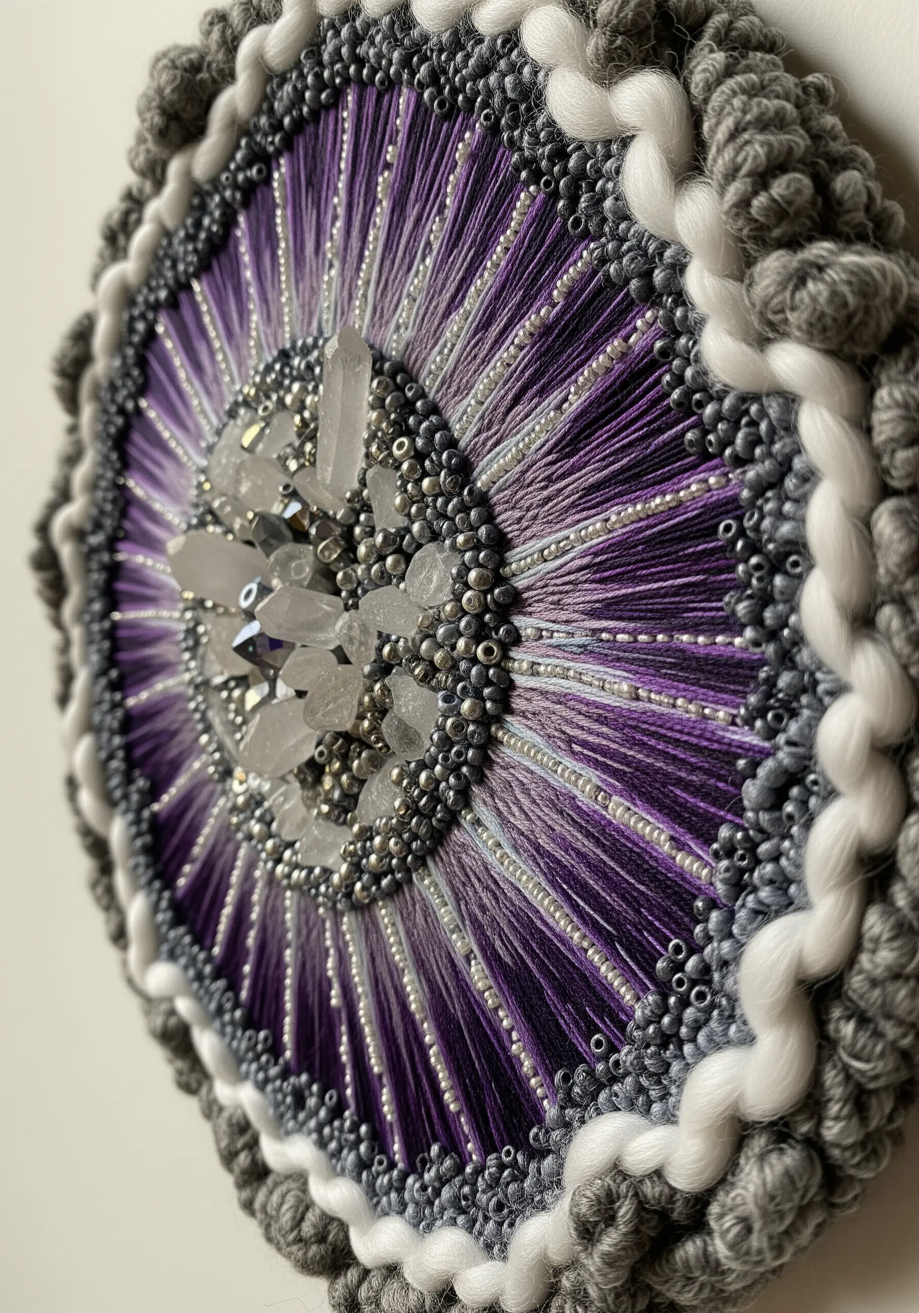 Mixed-media embroidery mandala with a central crystal cluster, beads, and purple threads.