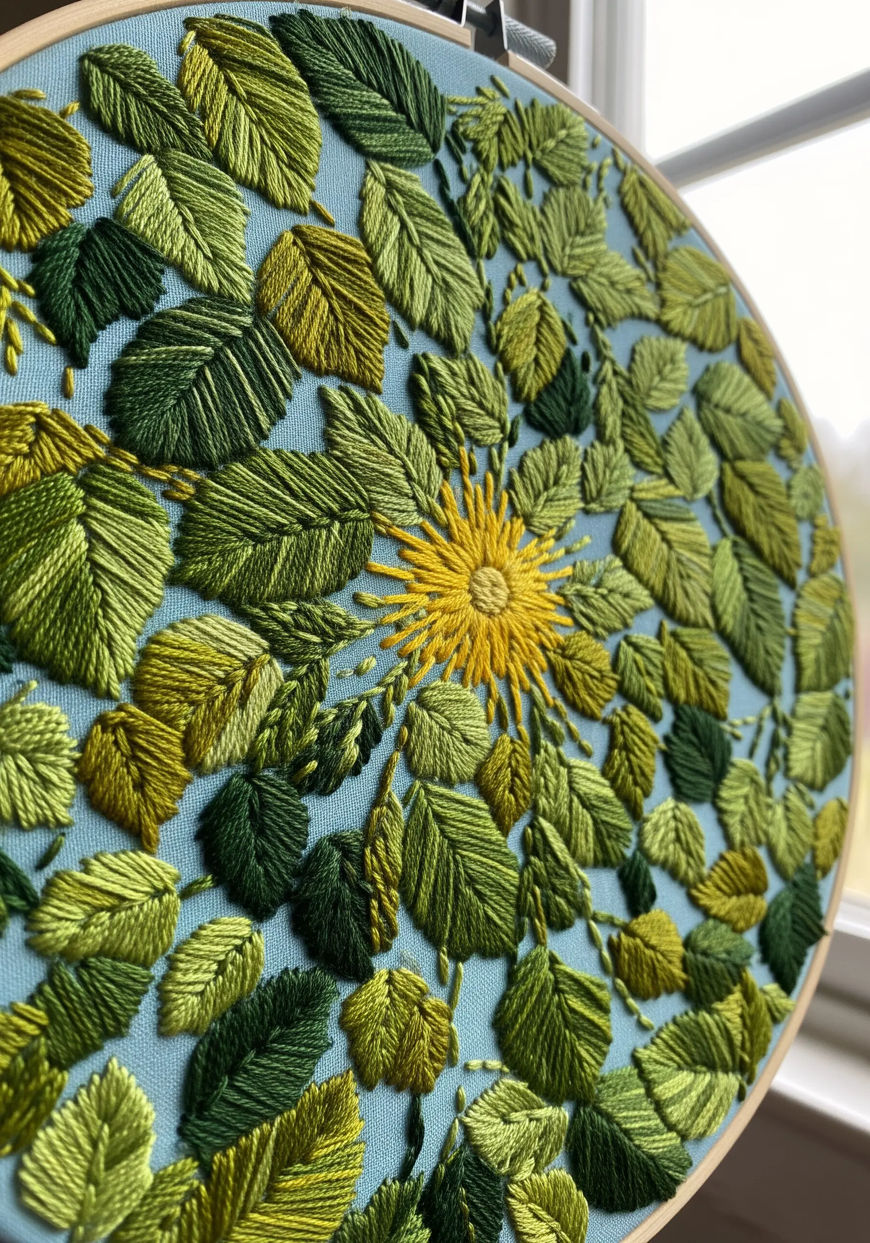 A dense circular pattern of green and yellow embroidered leaves, layered for a 3D effect.
