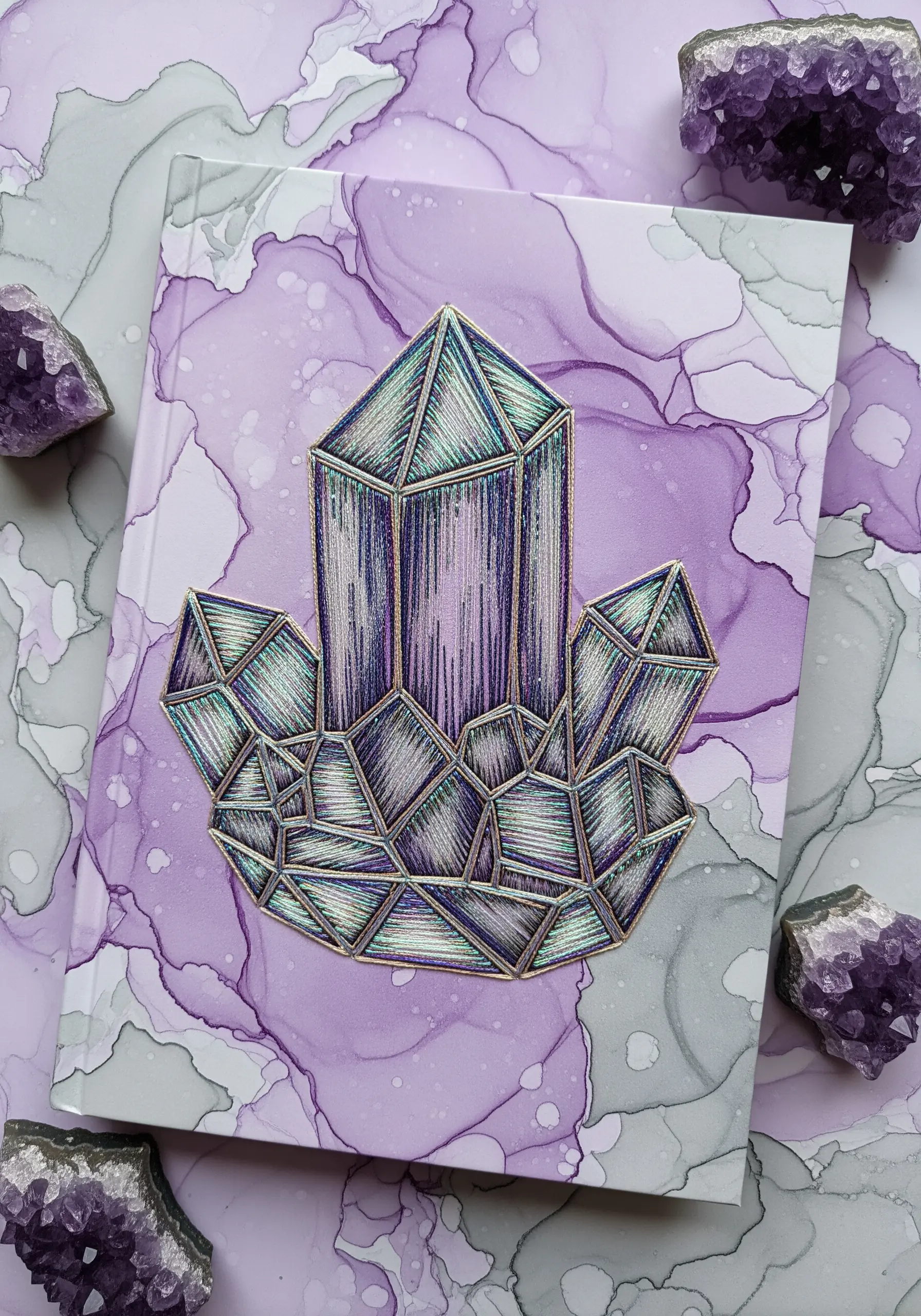 An embroidered crystal cluster in shades of purple with metallic outlines on a marbled background.