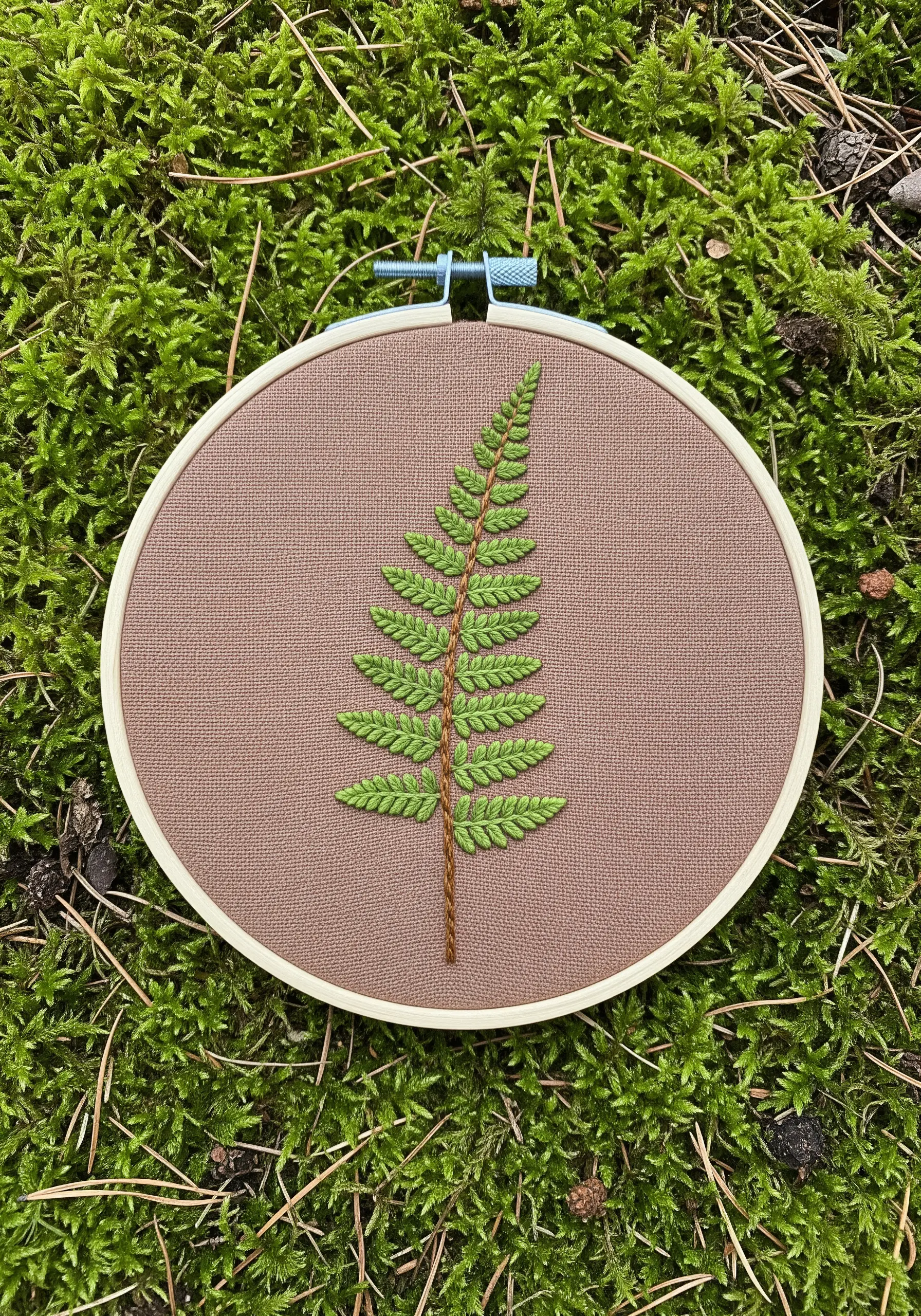 A single, elegant fern frond embroidered in green on brown fabric