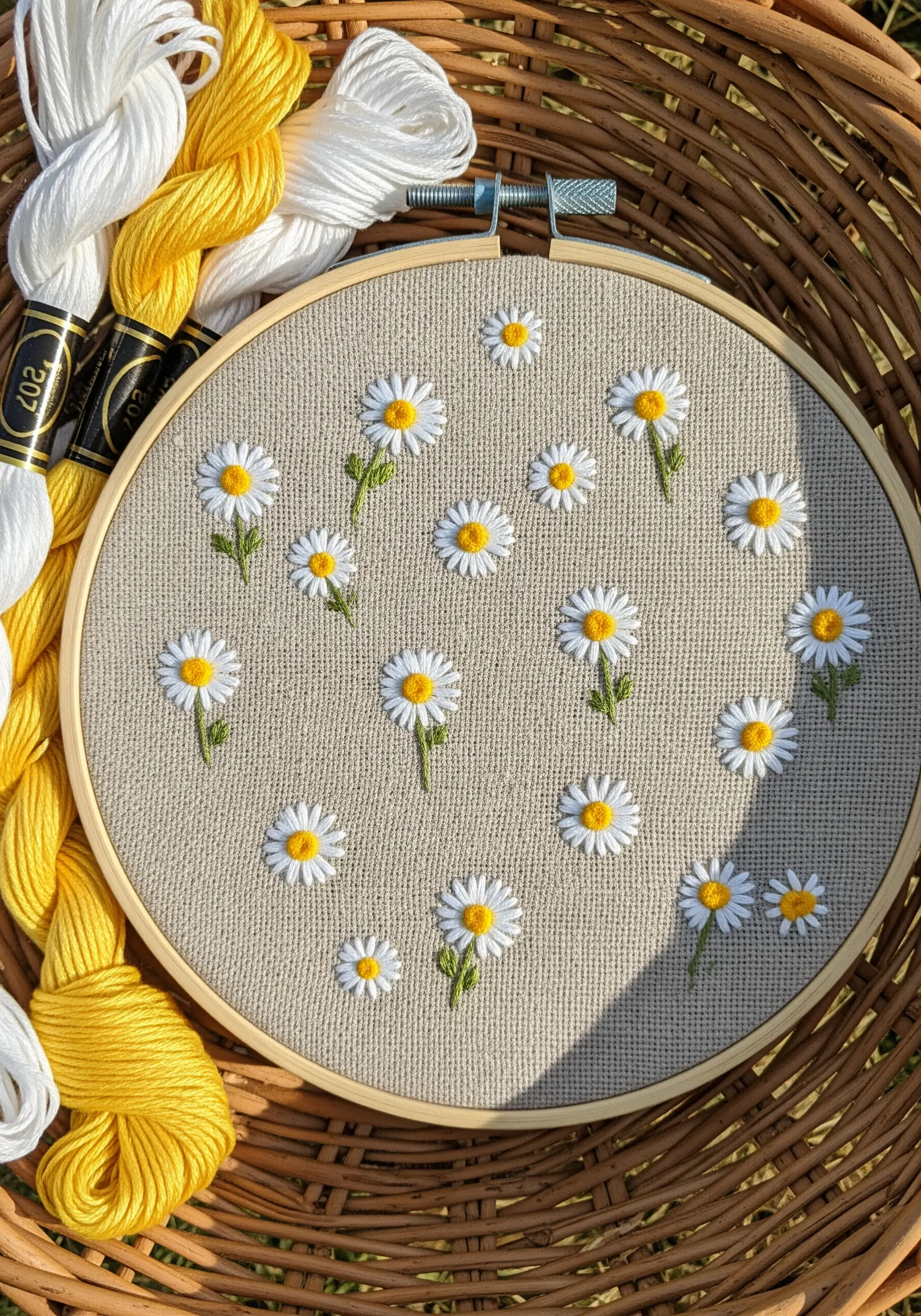 Embroidery of a scattered field of daisies with yellow centers on a neutral linen fabric.