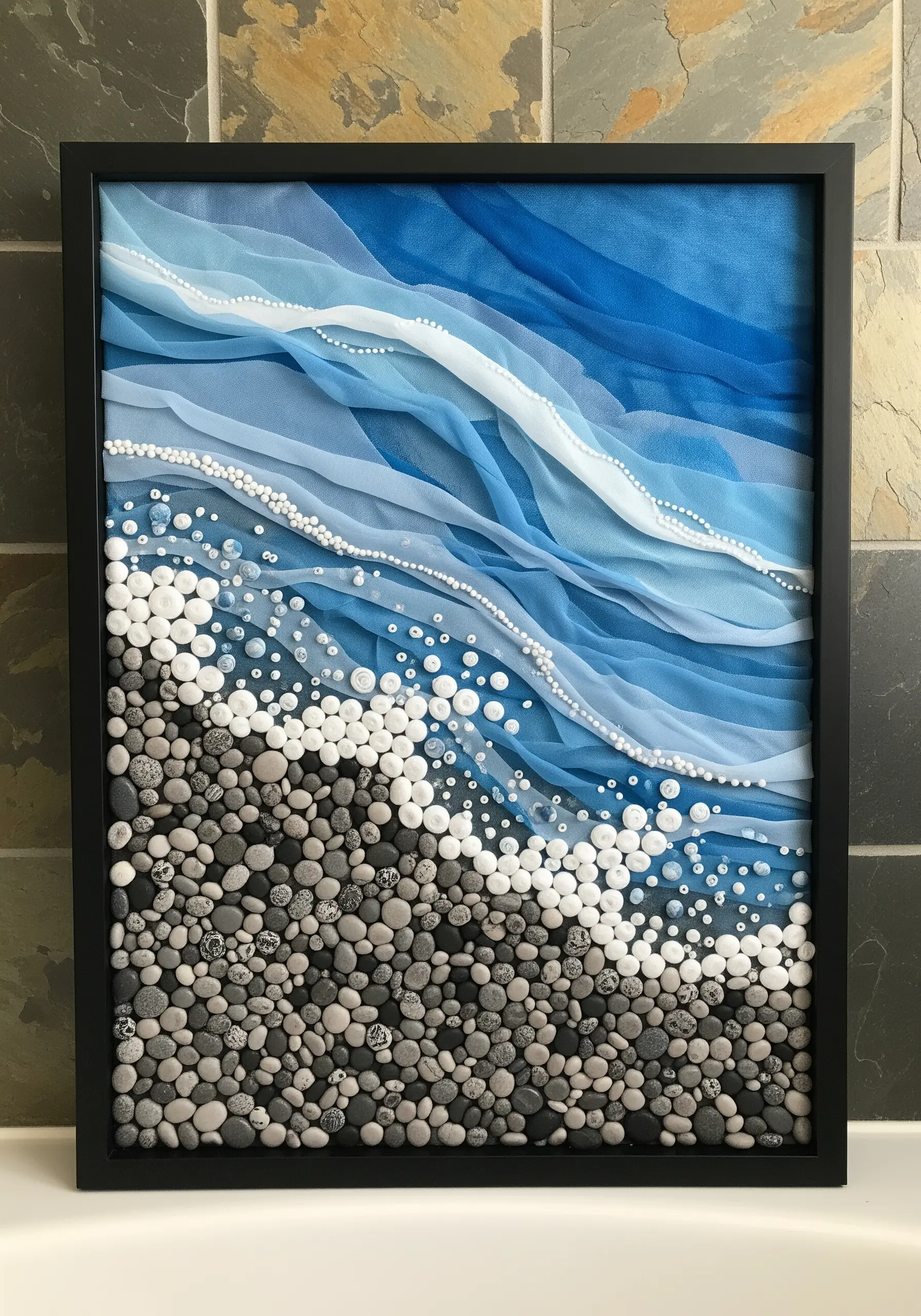 A mixed-media beach scene with a rocky shore made of real pebbles and waves of sheer blue fabric.
