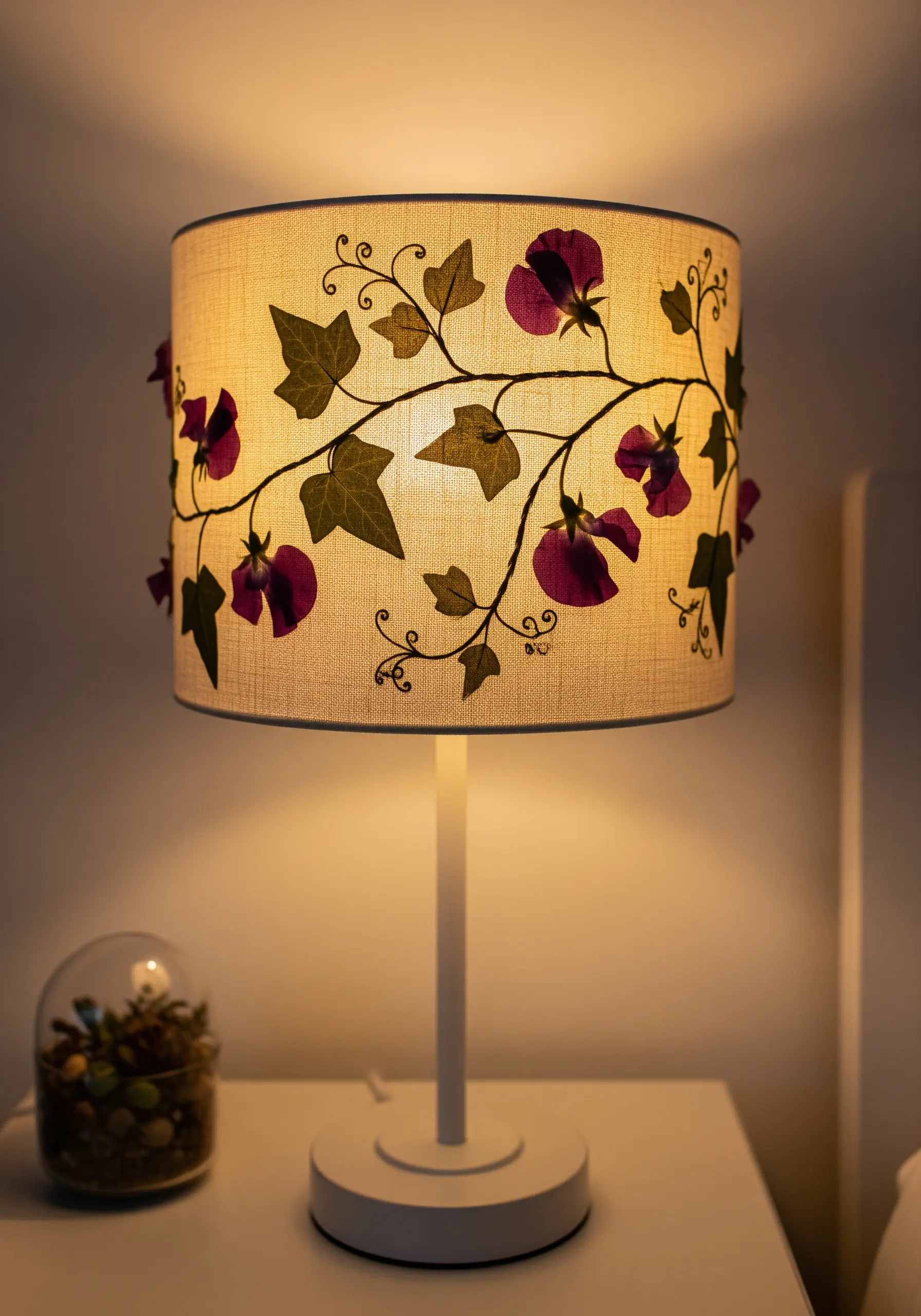 A linen lampshade decorated with stitched vines and pressed flowers, glowing warmly in a room.