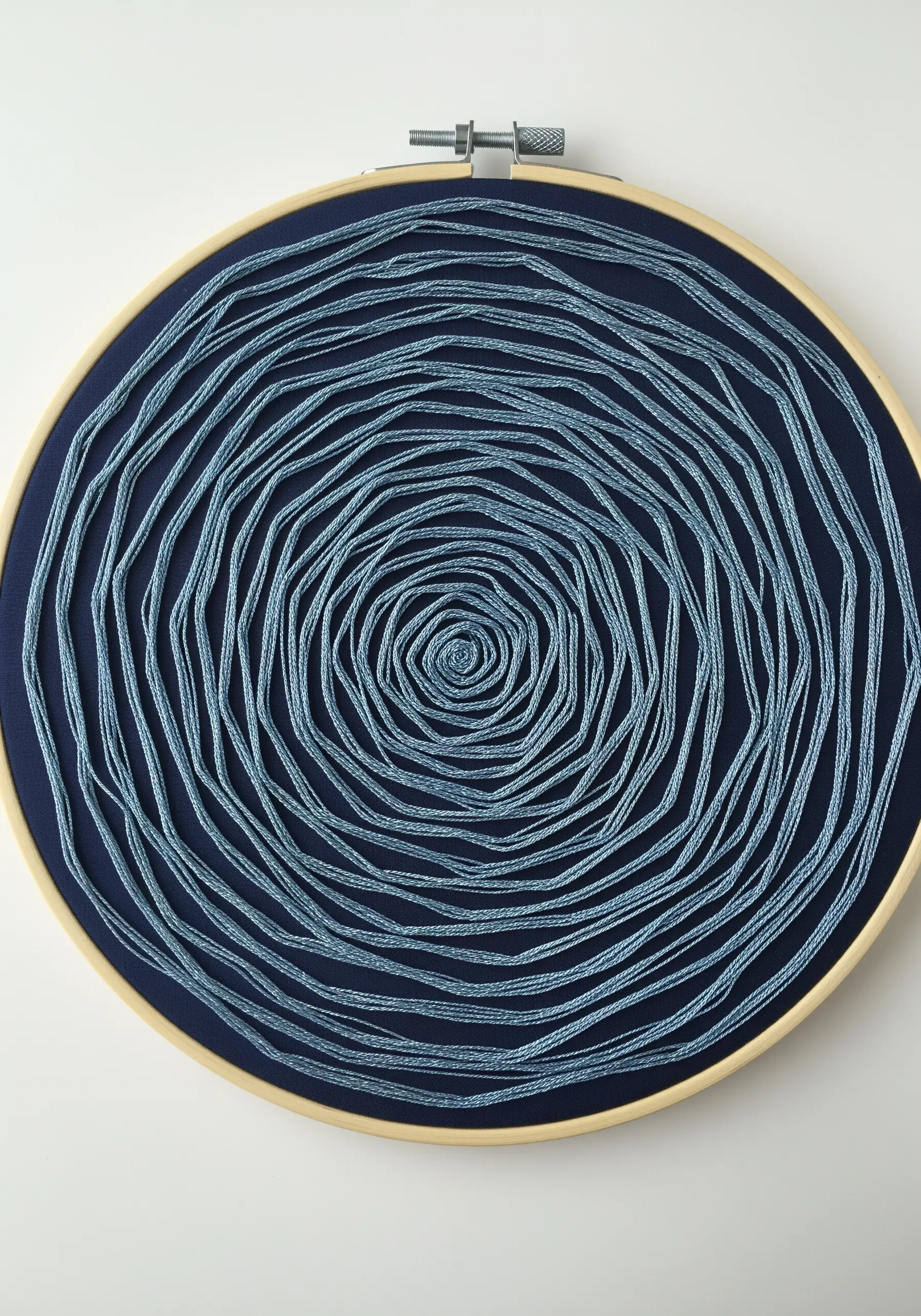 A continuous, organic spiral of couched blue metallic cord on a dark blue background.