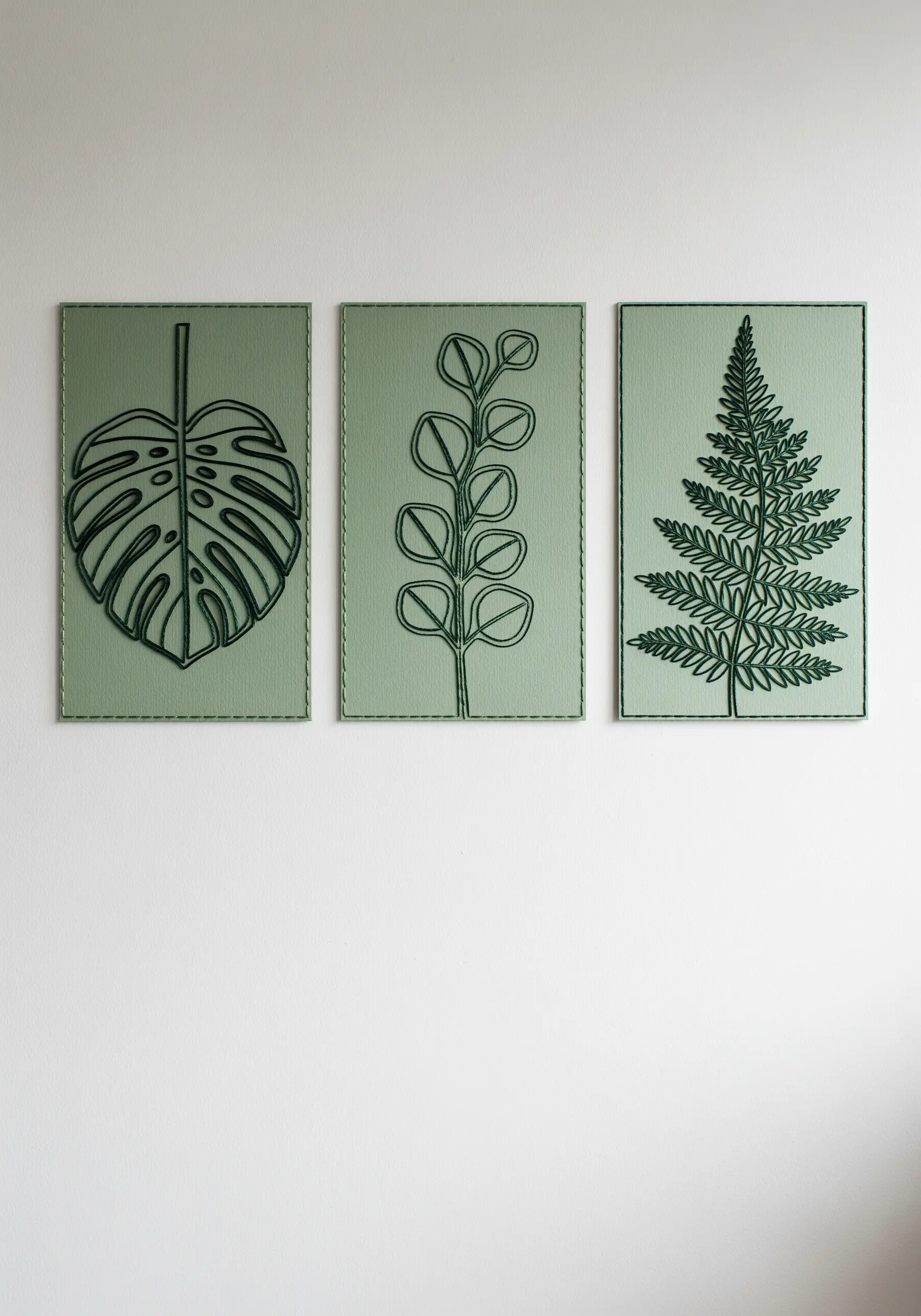 A set of three sage green paper panels with dark green machine-stitched botanical outlines.