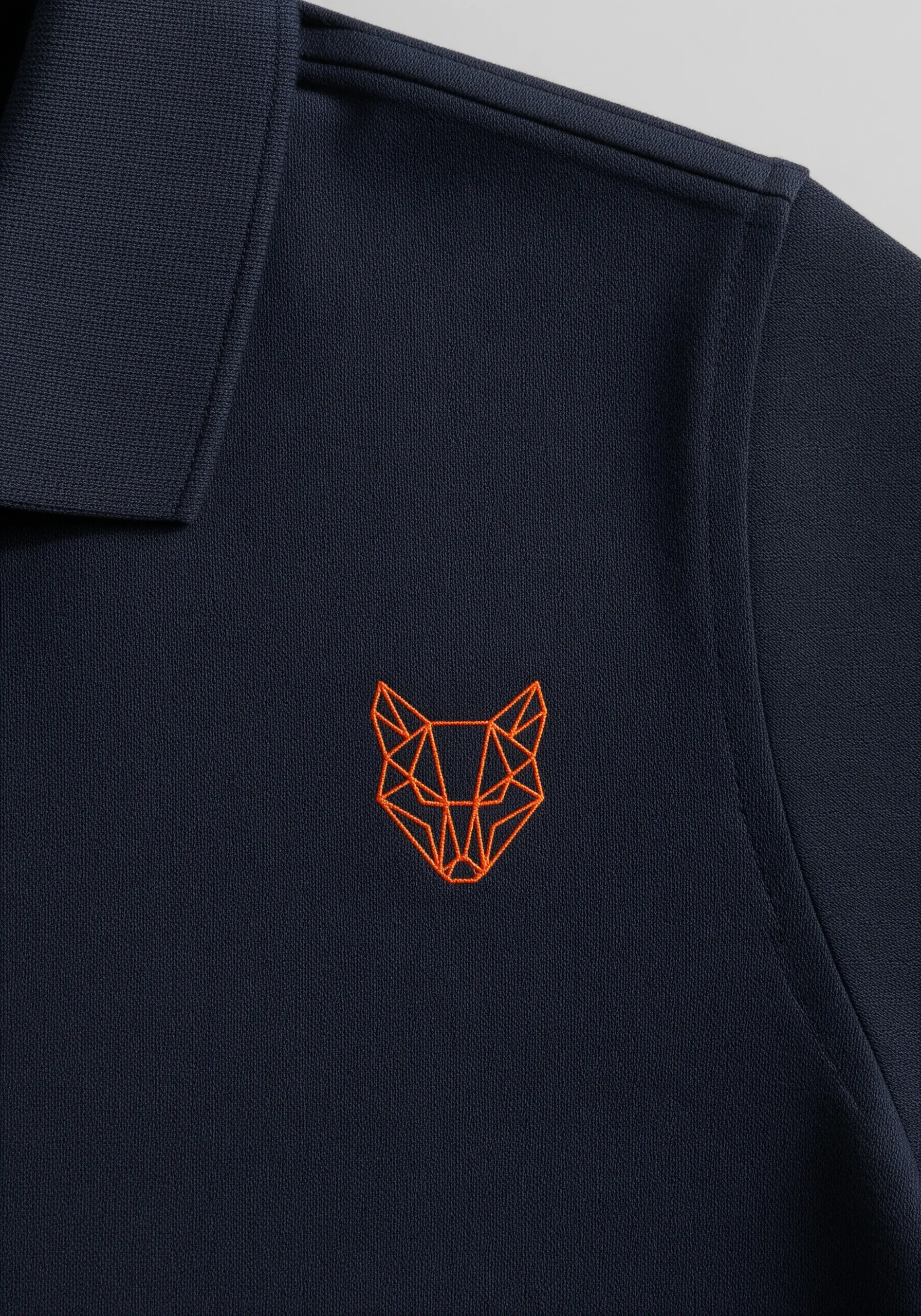 Geometric orange fox head outline embroidered on a navy blue polo shirt.