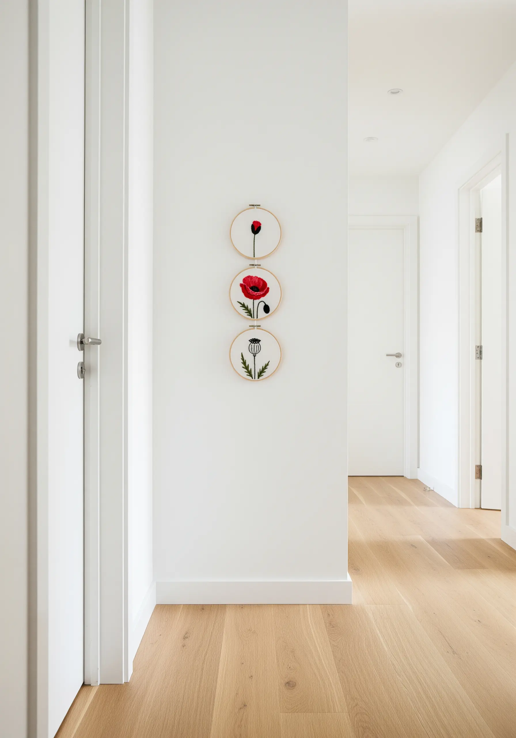 Three small embroidery hoops hung vertically, showing the life cycle of a poppy.