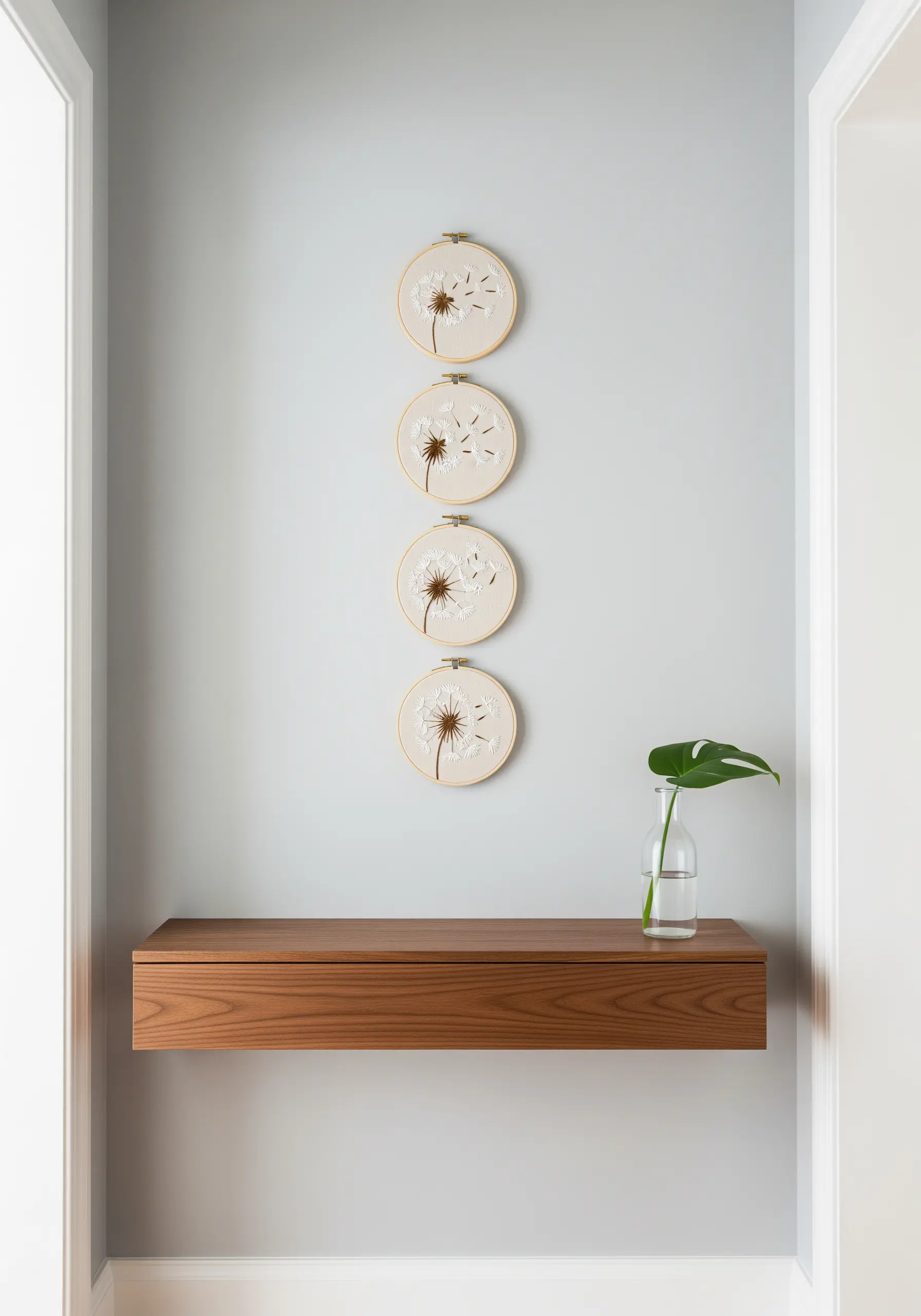 A vertical series of four embroidery hoops showing a dandelion losing its seeds.