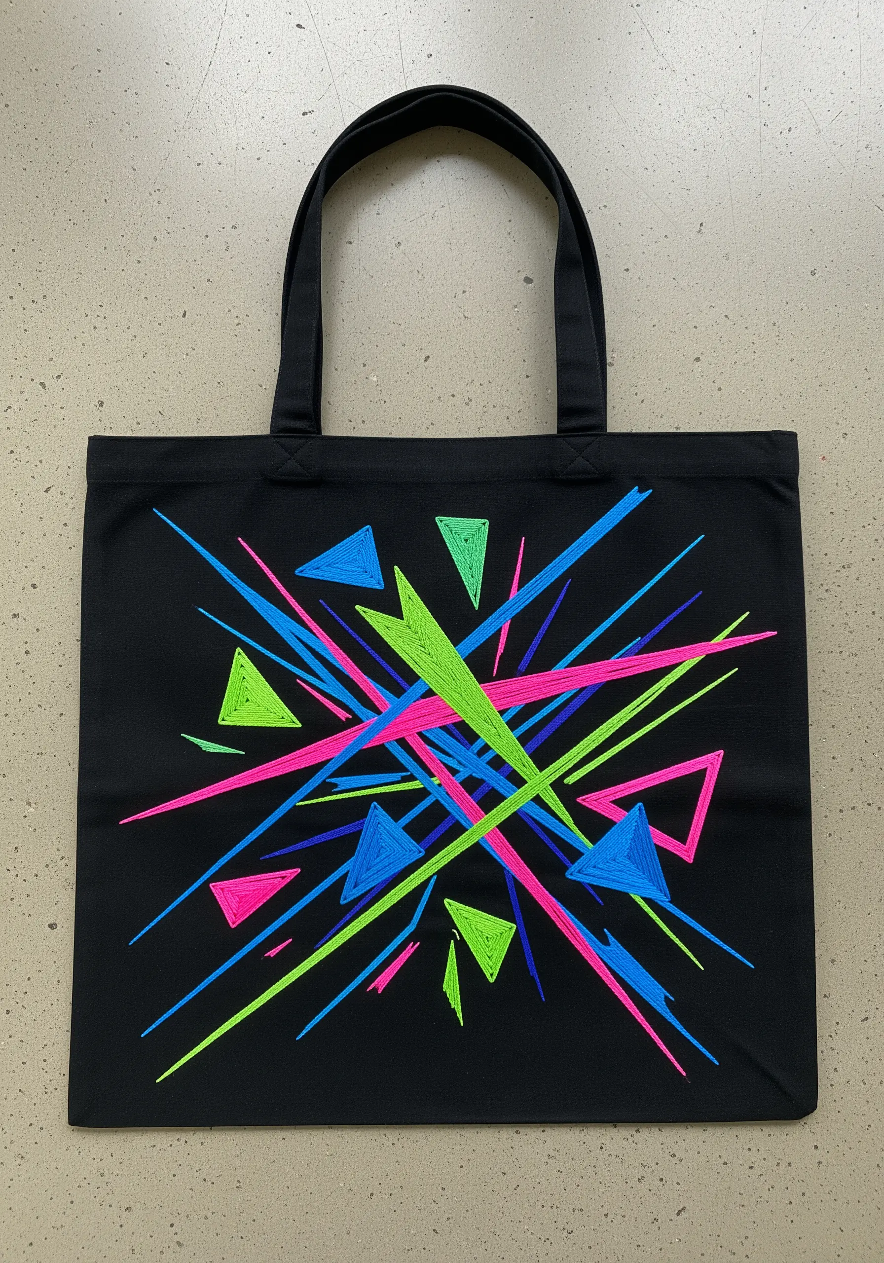 Abstract neon geometric embroidery with triangles and intersecting lines on a black tote bag.