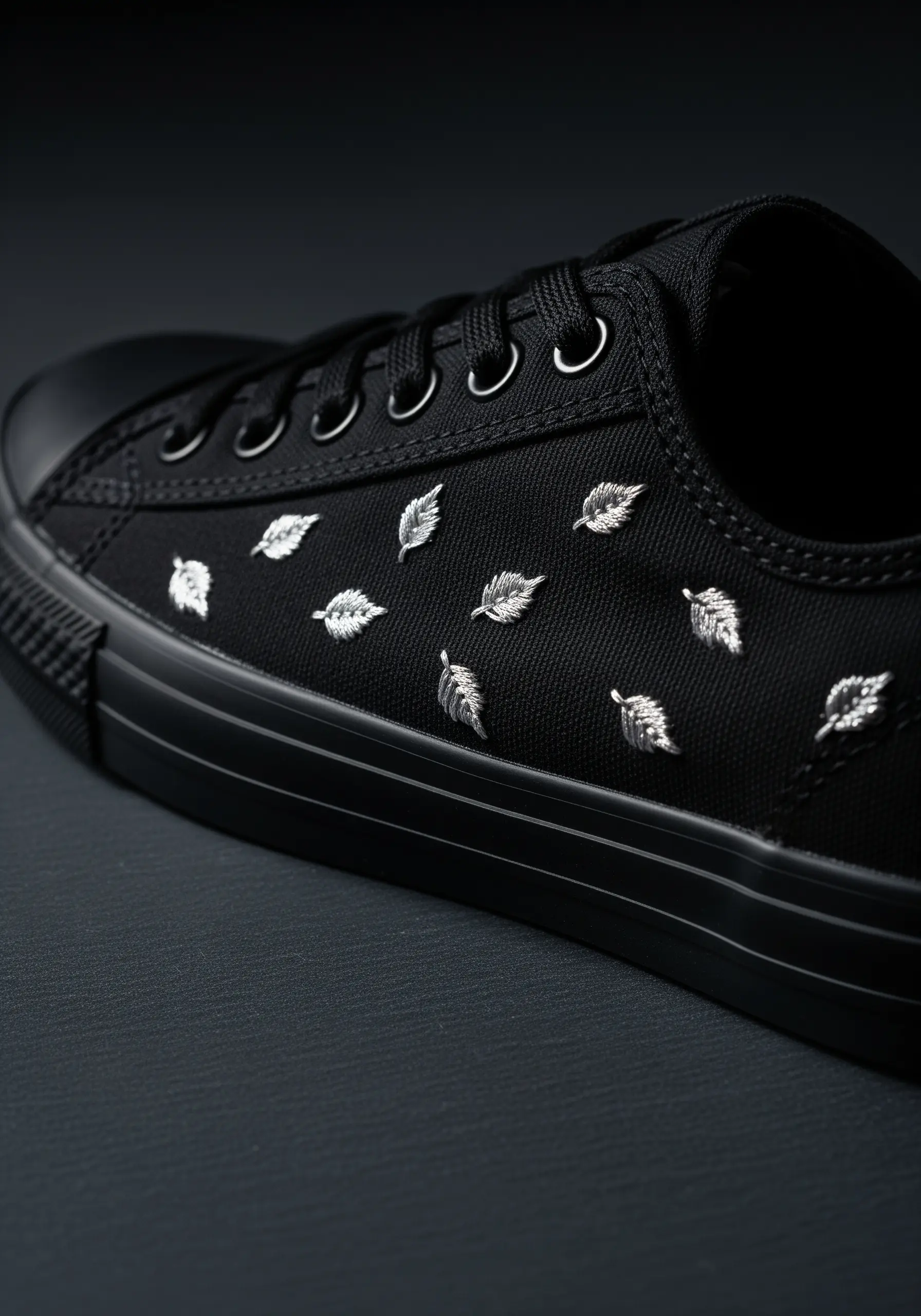 Small, scattered silver metallic leaves embroidered on the sides of black canvas sneakers.