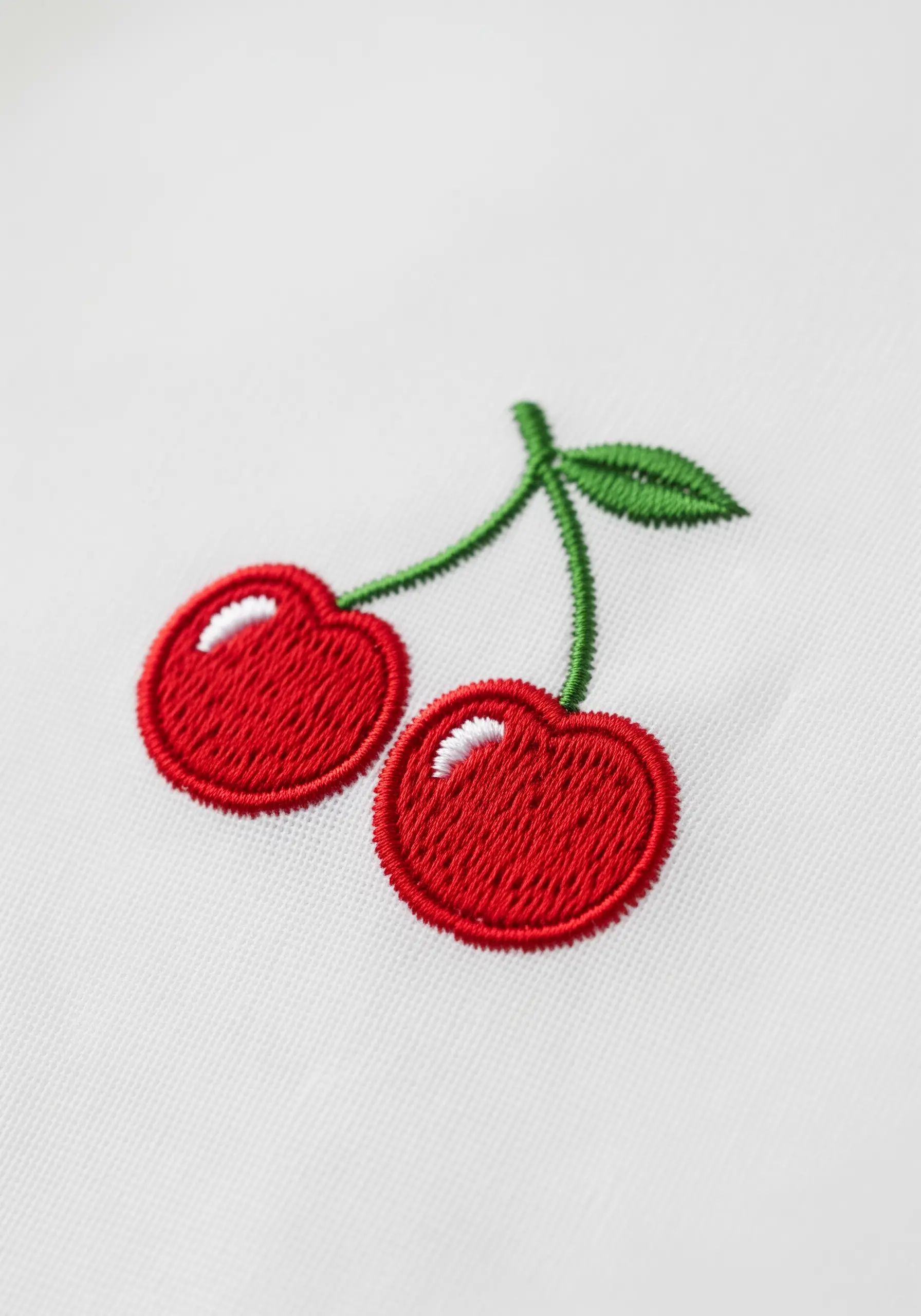 Two vibrant red embroidered cherries with green leaves and stems.