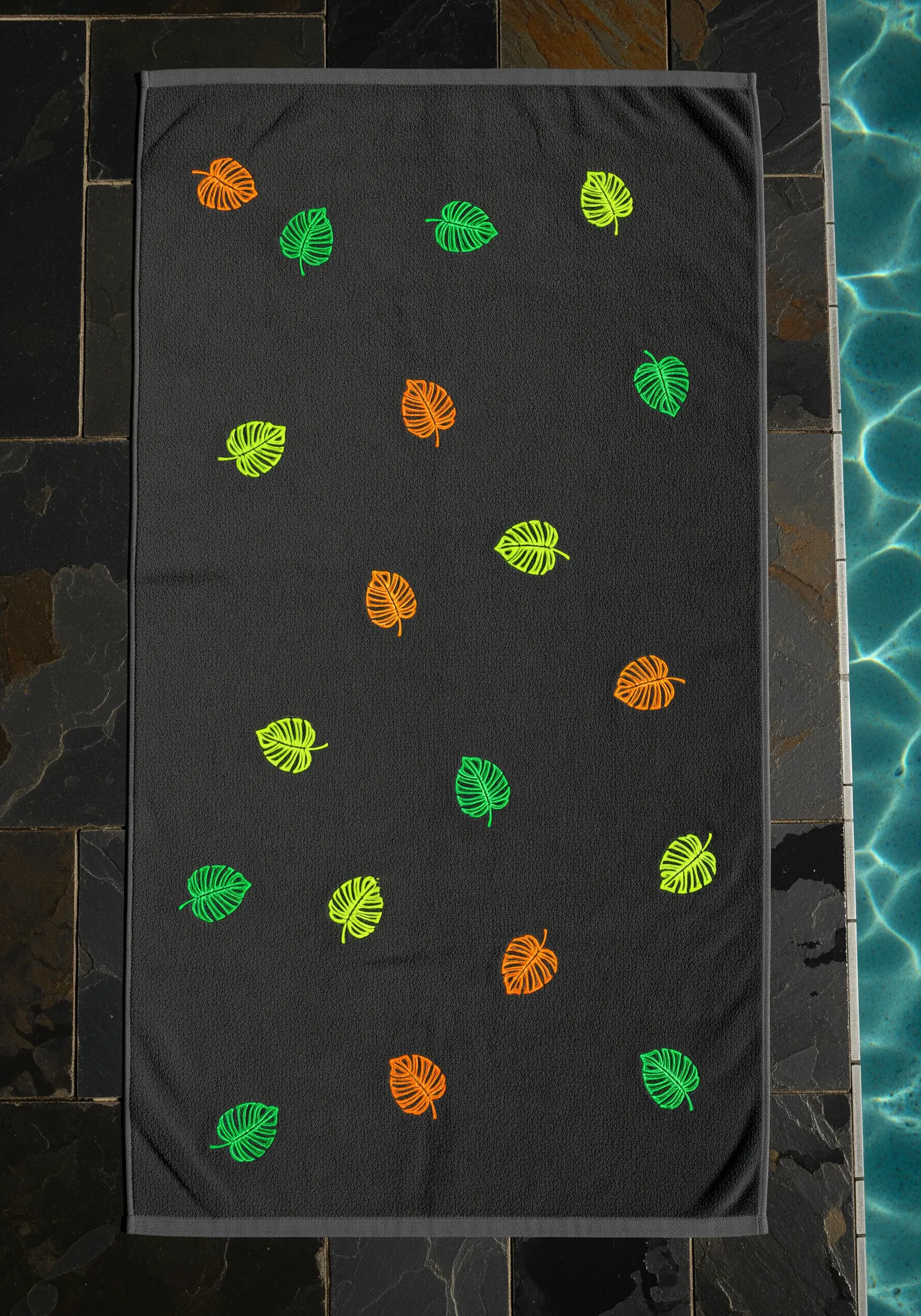 A dark grey towel with a scattered pattern of small monstera leaves in neon green, yellow, and orange.