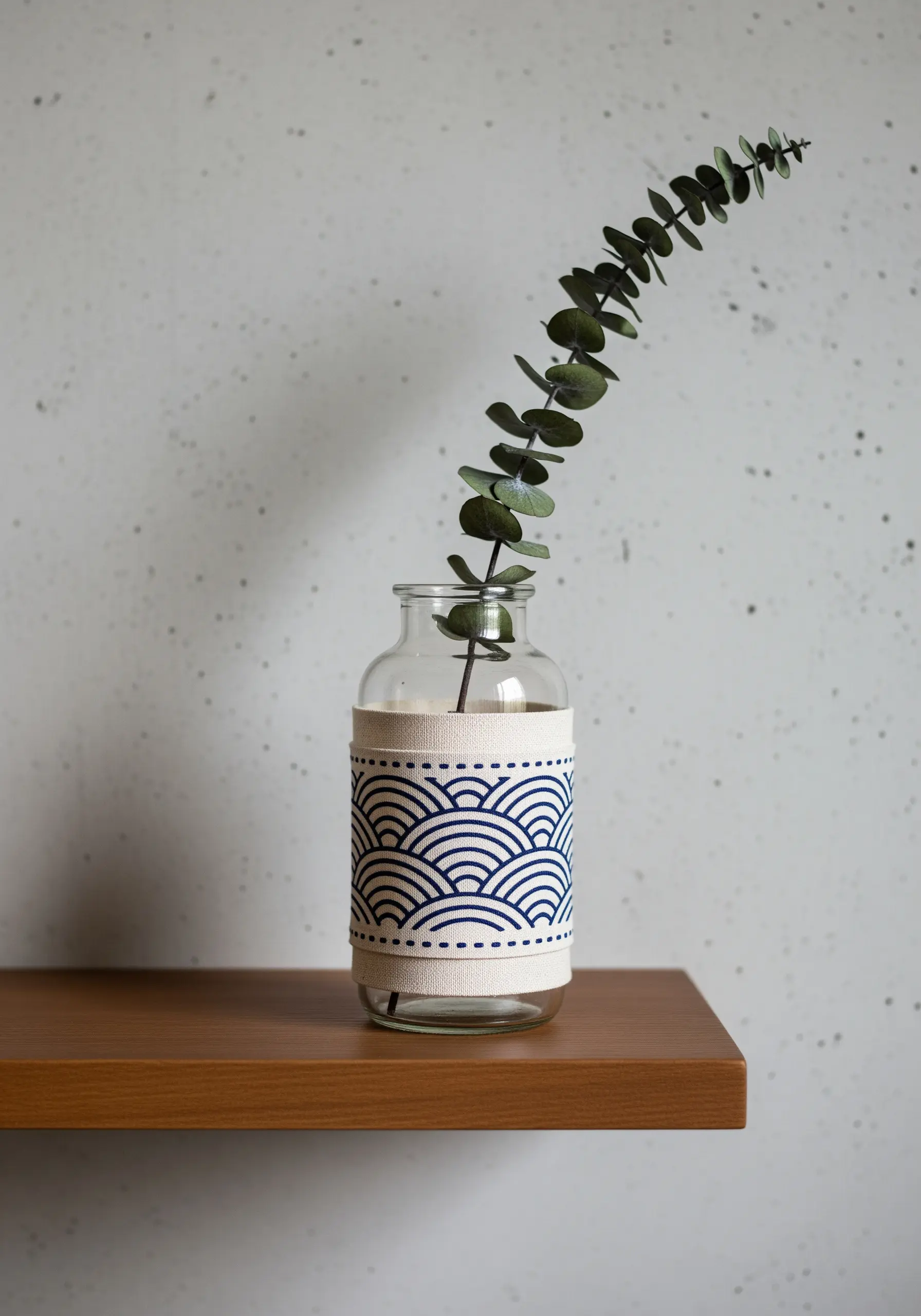 A glass vase decorated with a canvas wrap embroidered with a blue Japanese wave pattern.