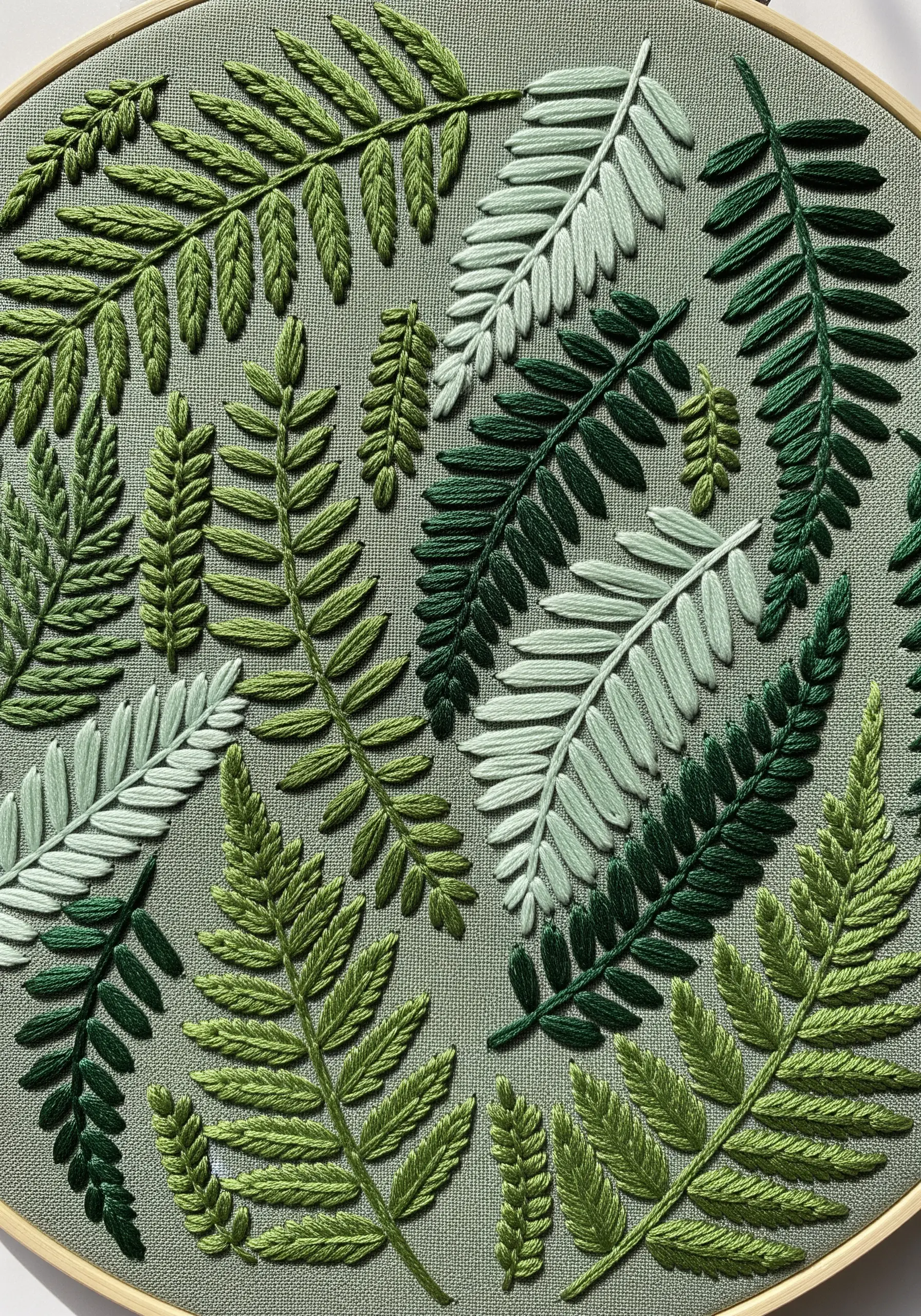 An embroidery hoop filled with various fern leaves stitched in different green textures.