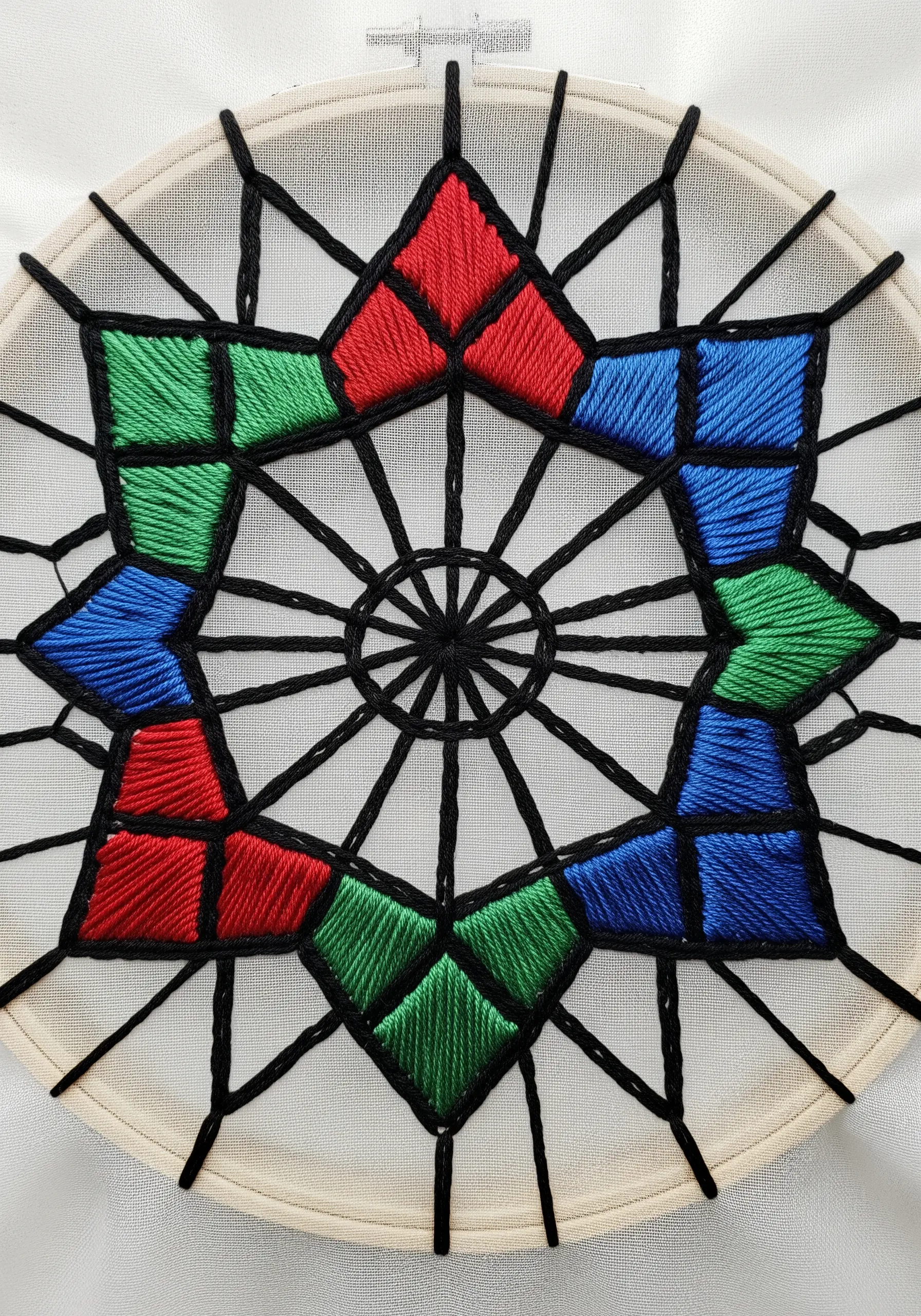 A geometric mandala with black outlines and red, green, and blue satin stitch fills.