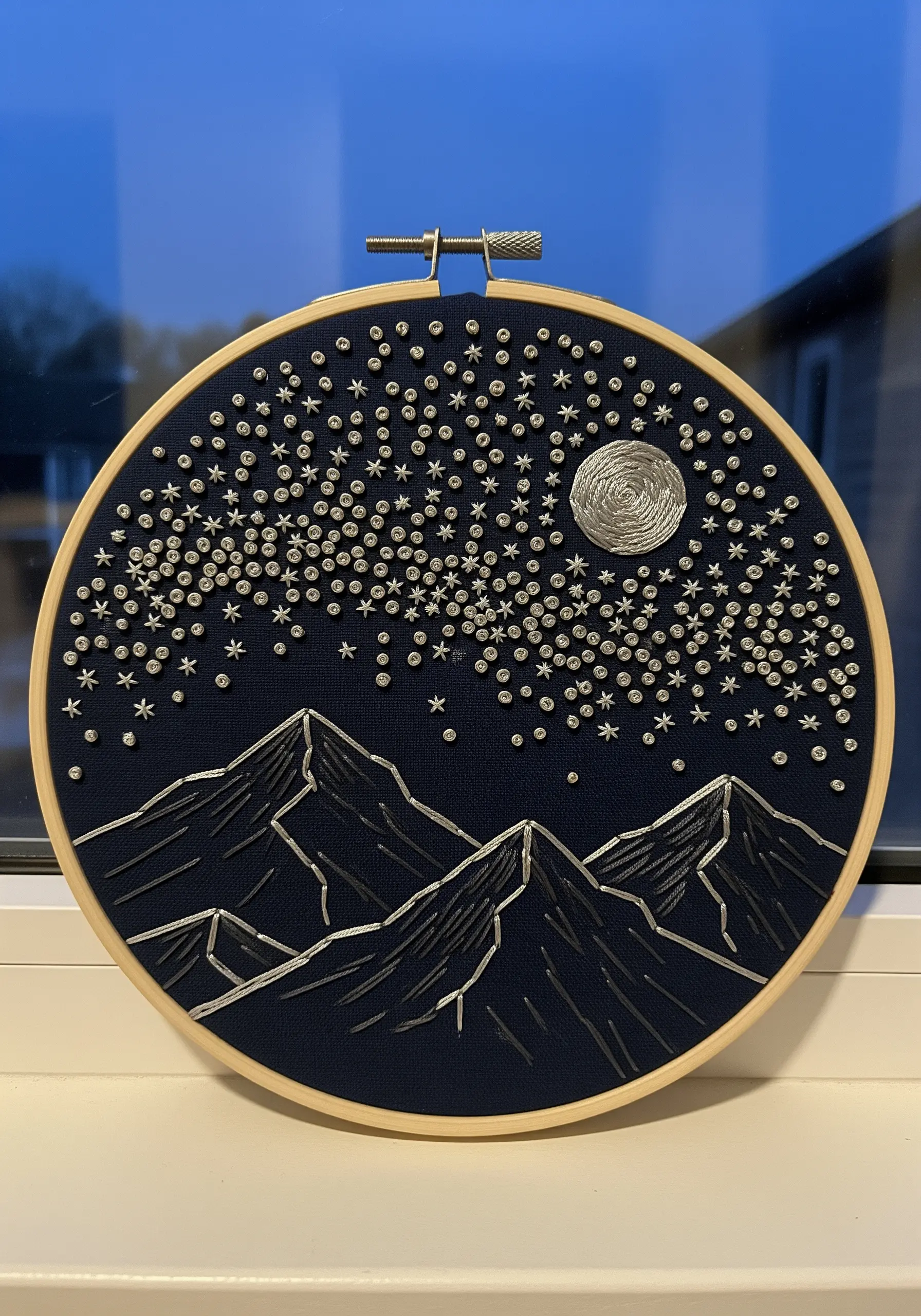 Night sky embroidery with a textured silver moon and a dense field of metallic stars over mountains.
