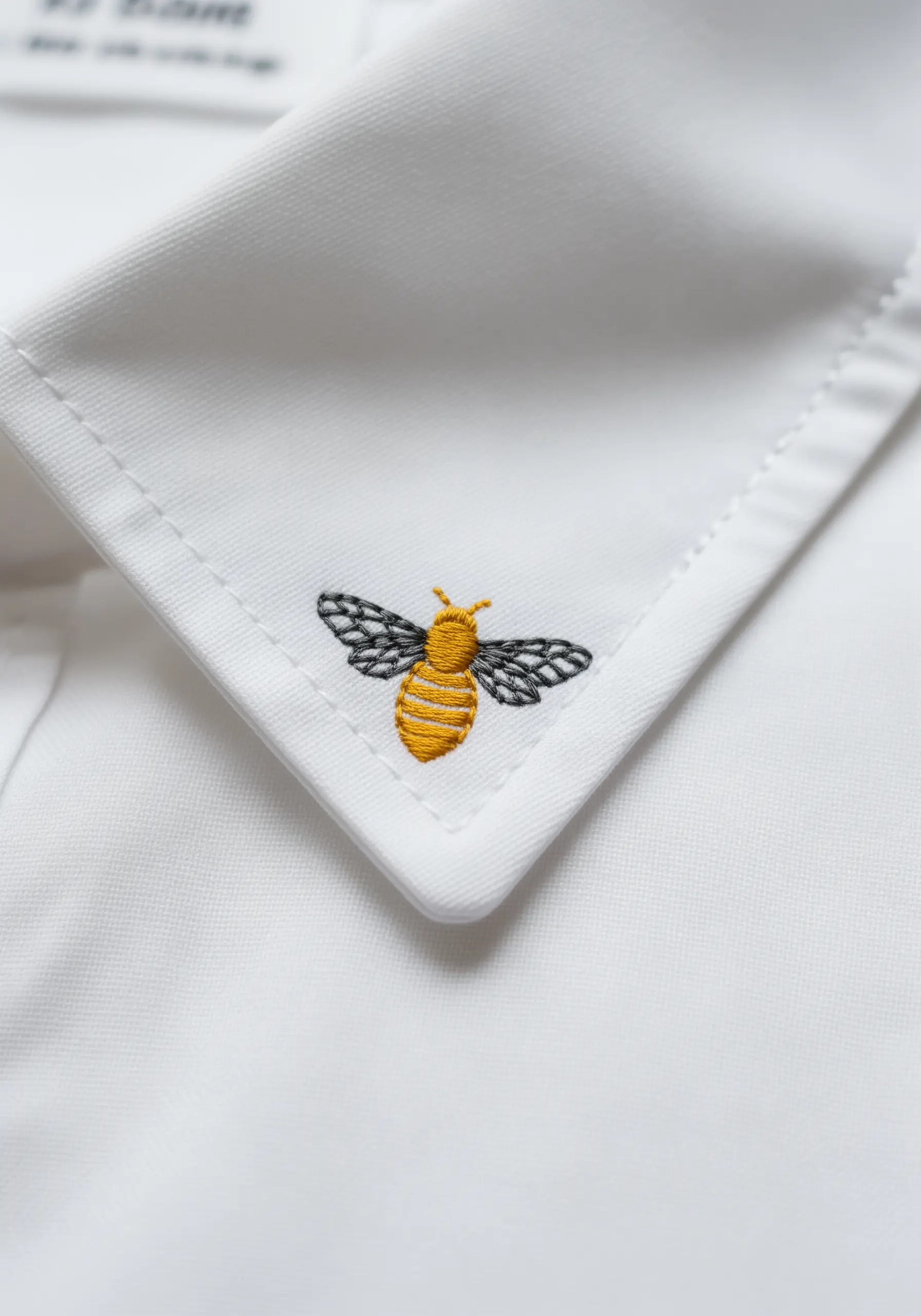 Tiny embroidered bee with detailed wings on the crisp white collar of a shirt.