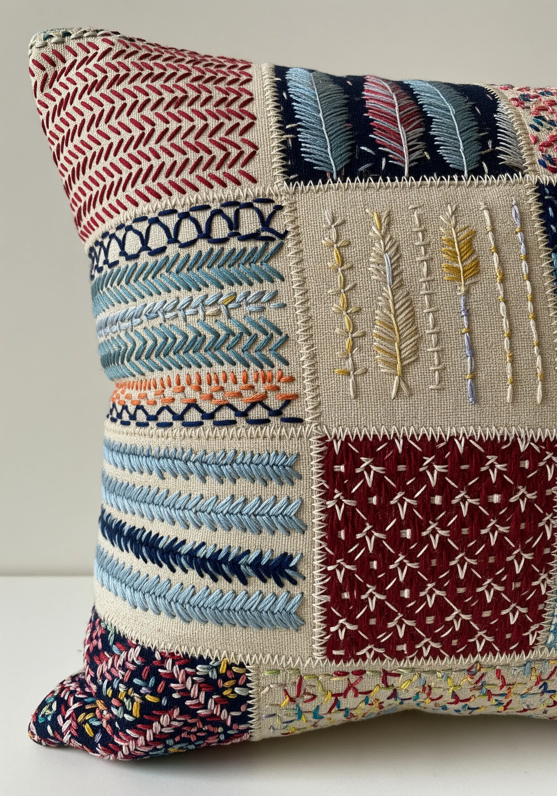 A patchwork cushion covered in squares of different embroidery stitch samples