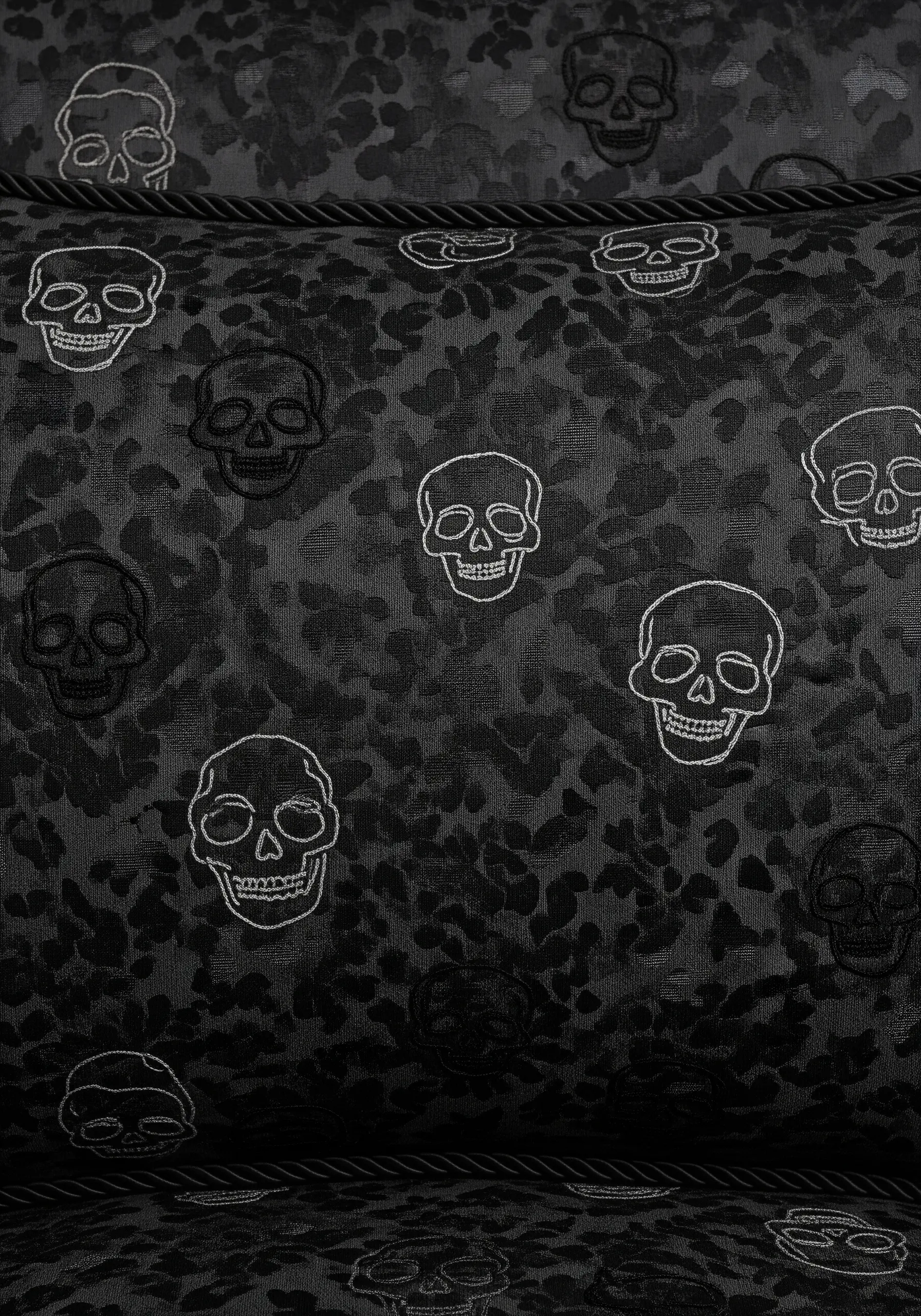 A repeating pattern of small skulls outlined in white thread on a black patterned fabric.