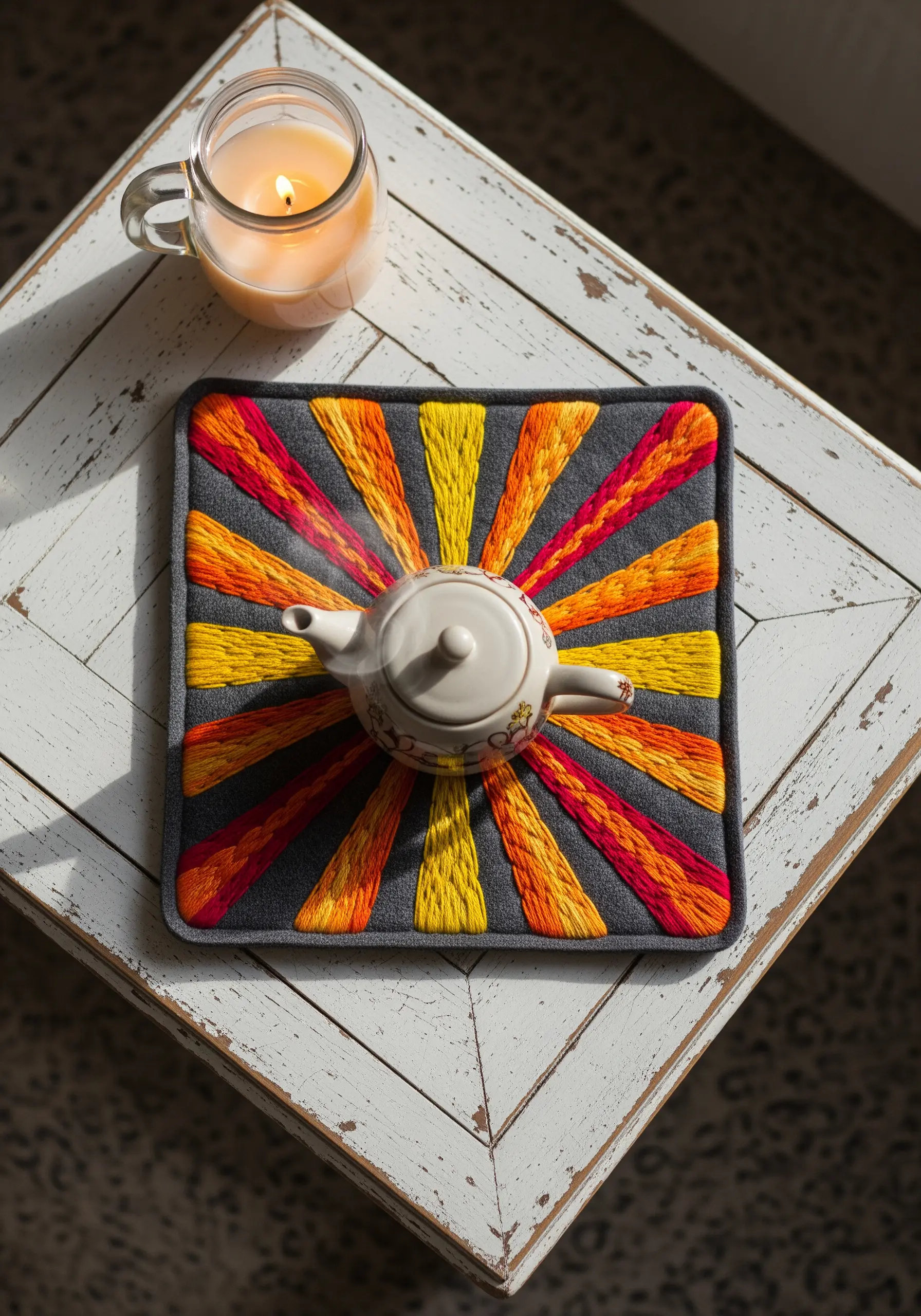 A square trivet embroidered with radiating sunburst rays in yellow, orange, and red.