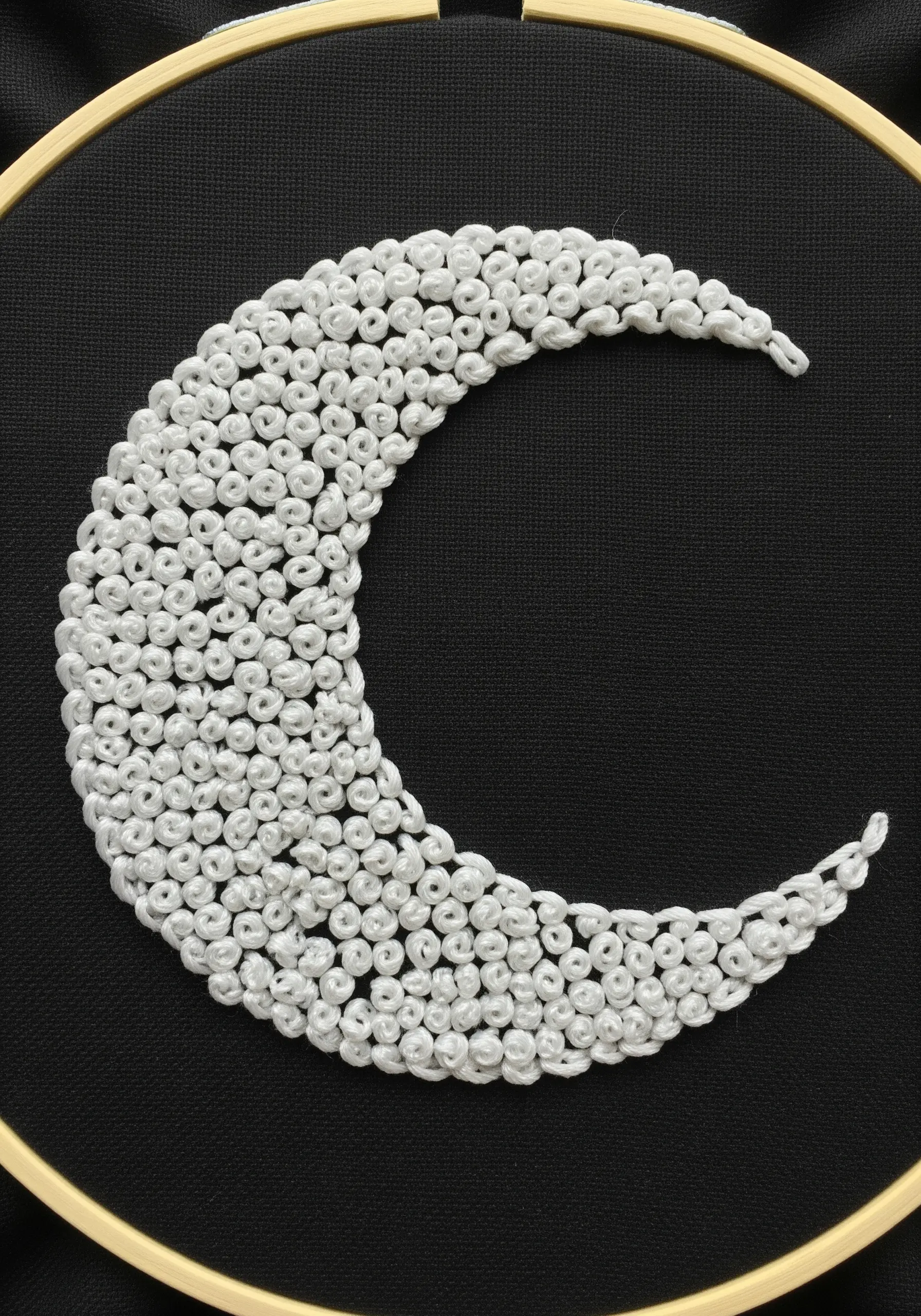Crescent moon filled entirely with white French knots on black fabric.