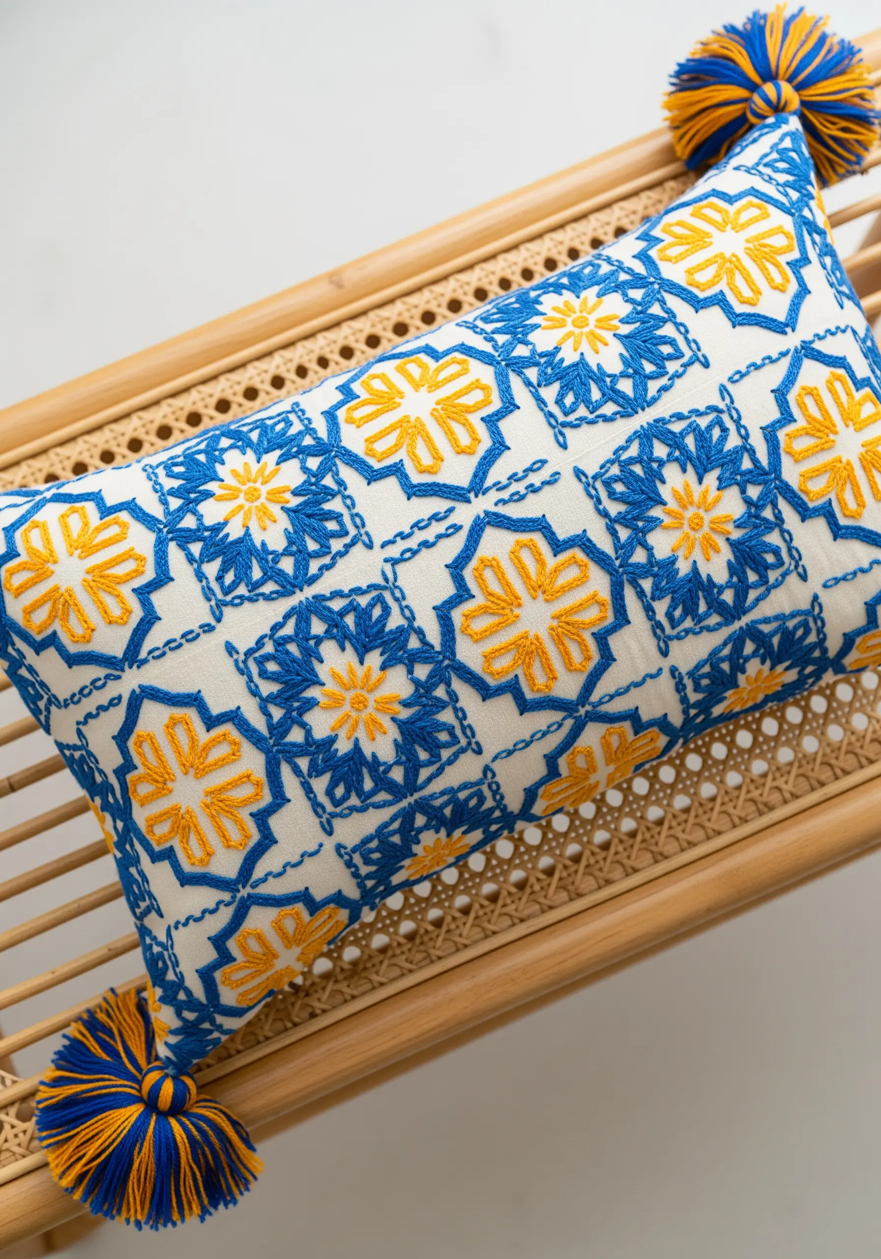 A cushion embroidered with a repeating blue and yellow tile-like pattern and matching tassels