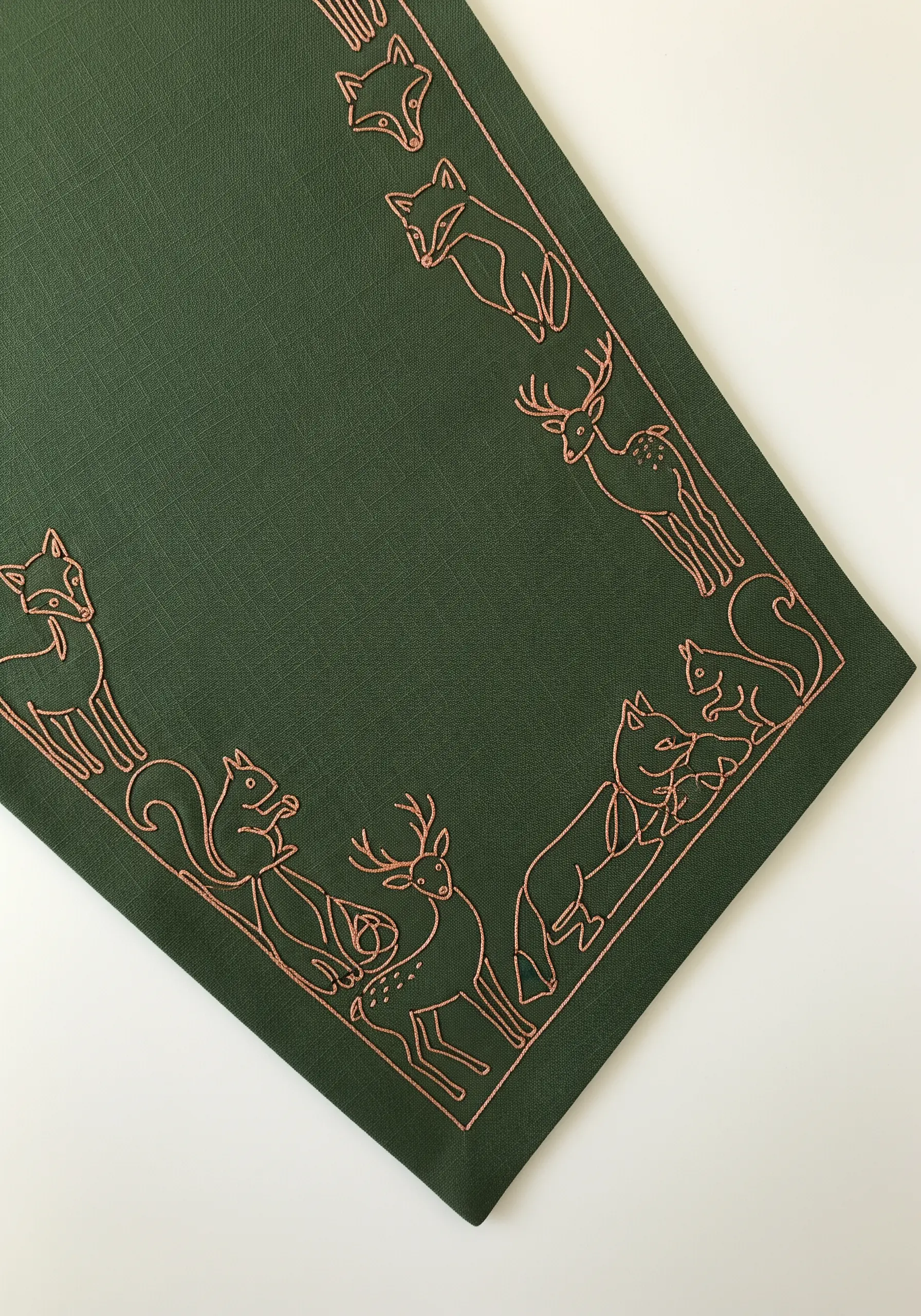 A border of woodland animals like foxes and deer outlined in copper thread on green fabric.