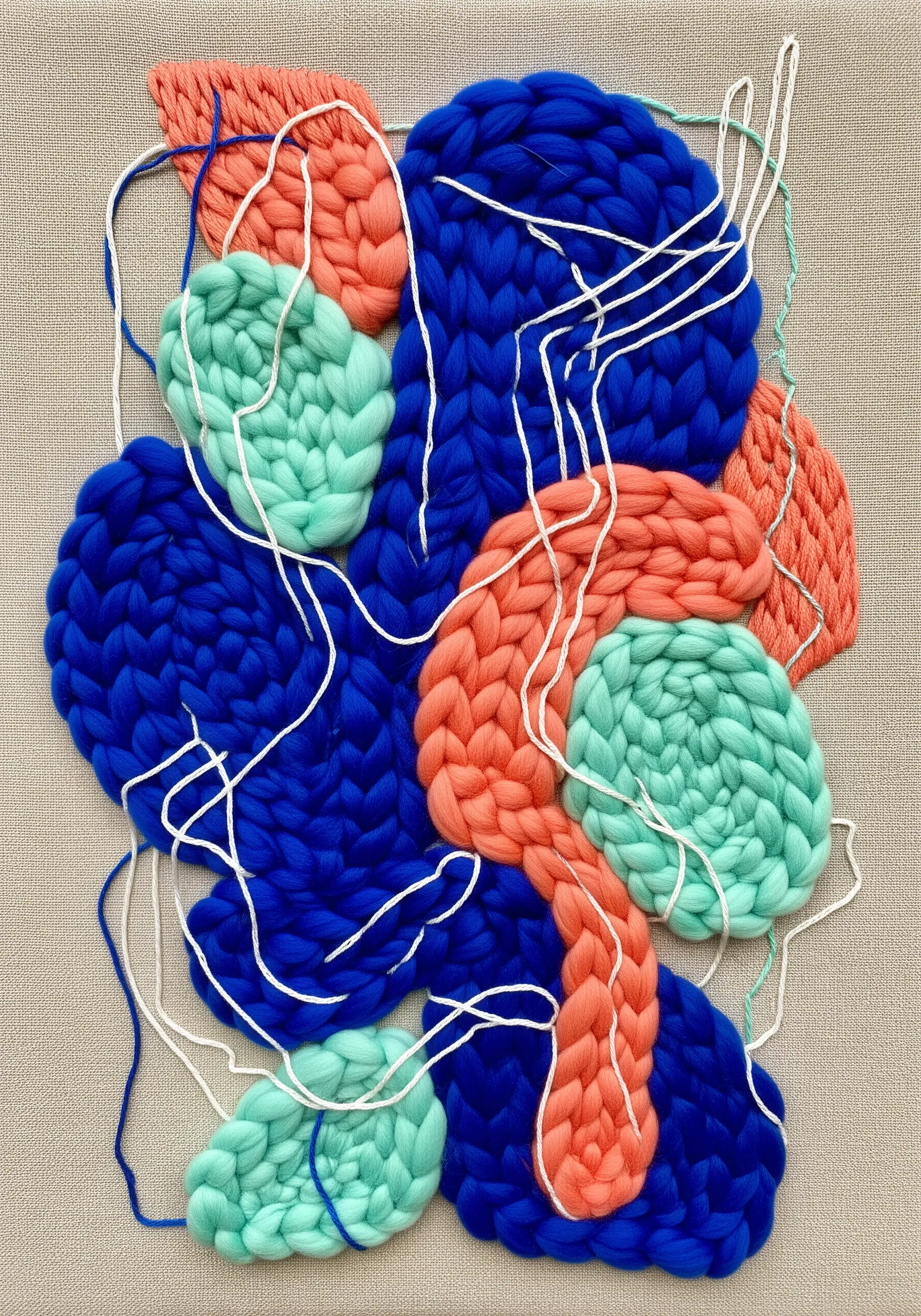 An abstract fiber art piece with chunky knitted shapes in blue, coral, and mint on a neutral canvas.