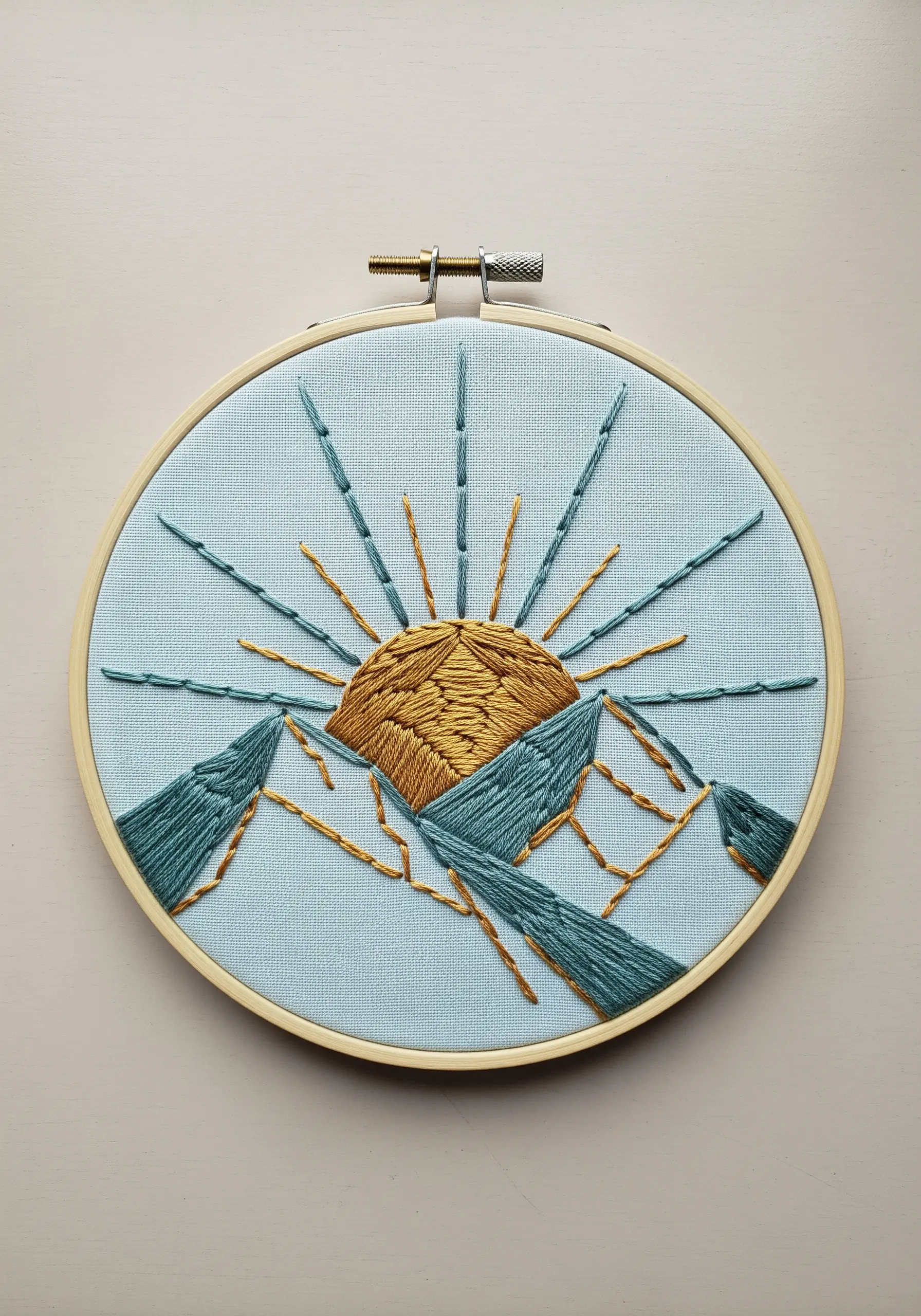 Abstract embroidery of a golden sun rising over teal-colored mountains.