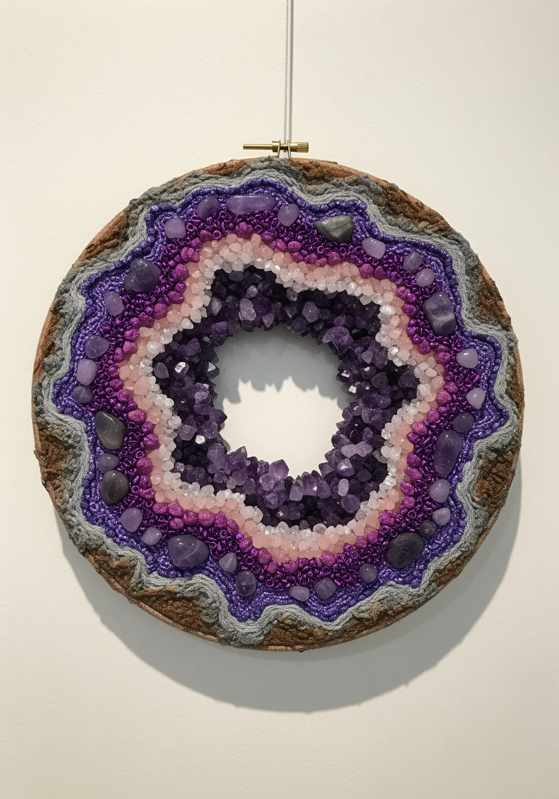 A hoop art piece of an amethyst geode, using real amethyst crystals, beads, and textured yarns.