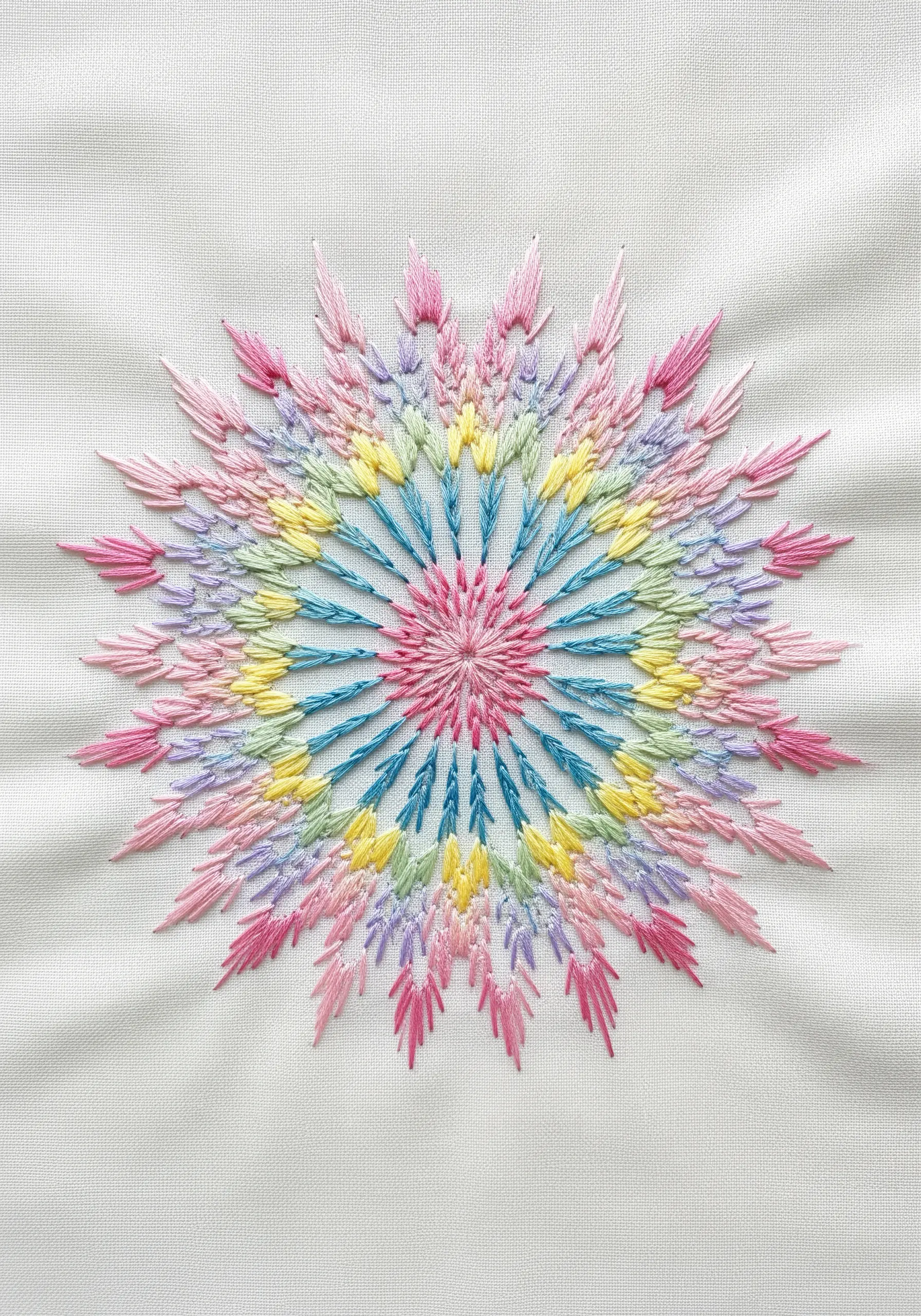 A starburst mandala in soft pastel colors using radiating feather or fly stitches.