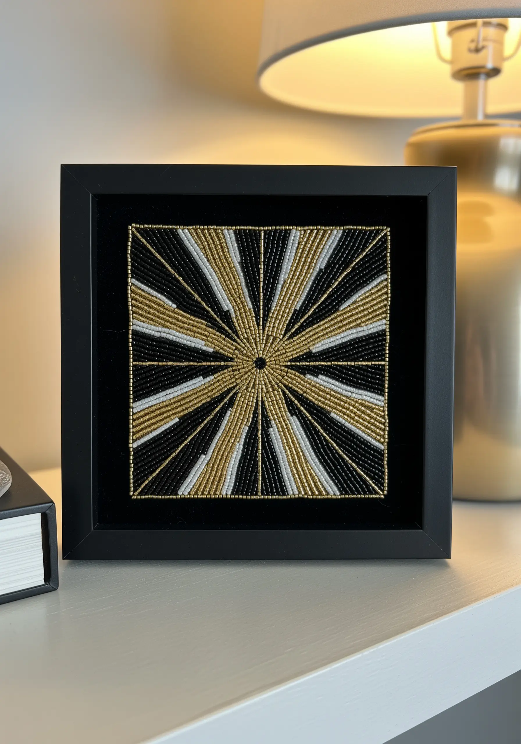 Framed geometric sunburst pattern made entirely of gold, black, and white seed beads.