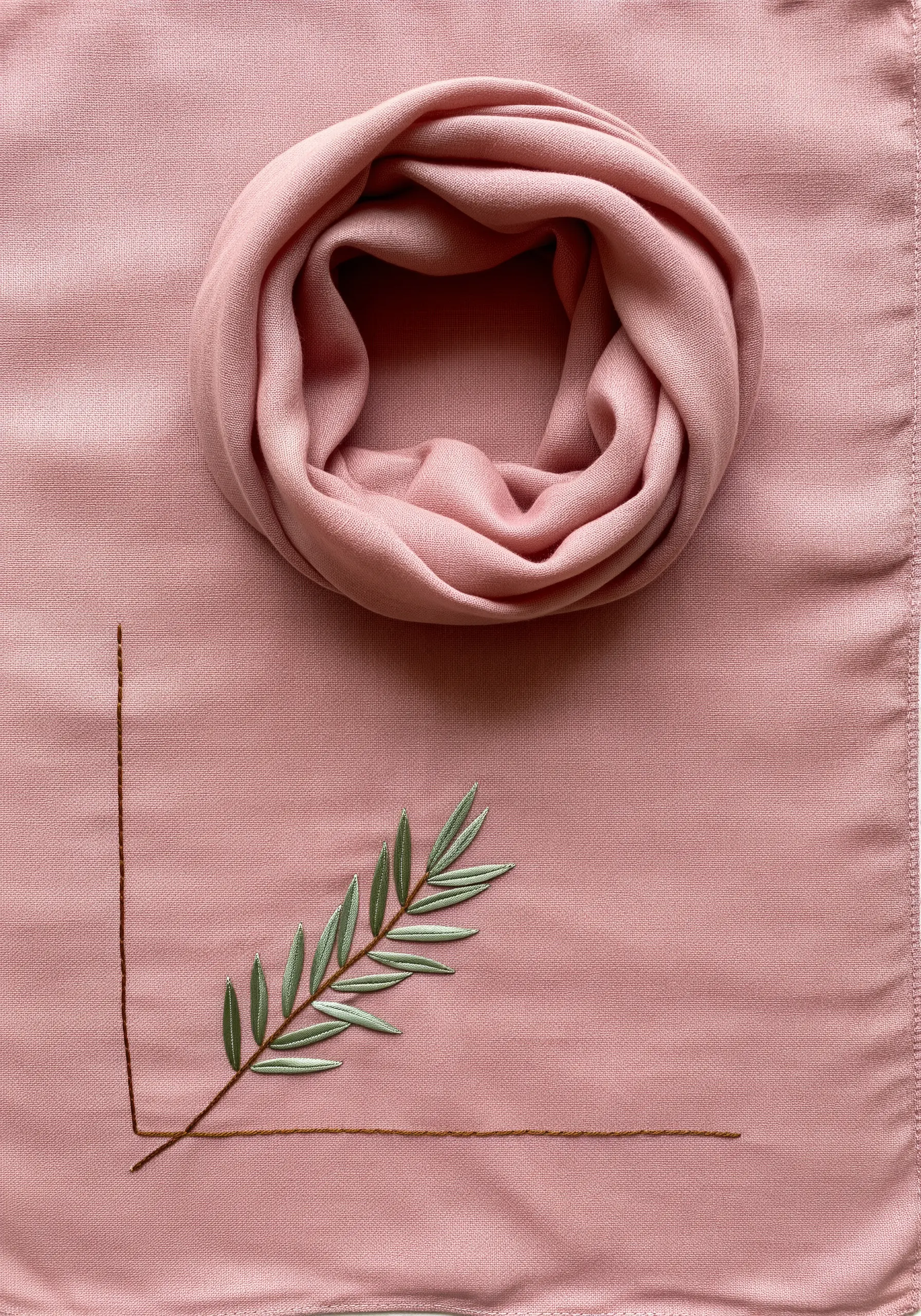 An olive branch with satin-stitched leaves framed by two intersecting lines on pink fabric.