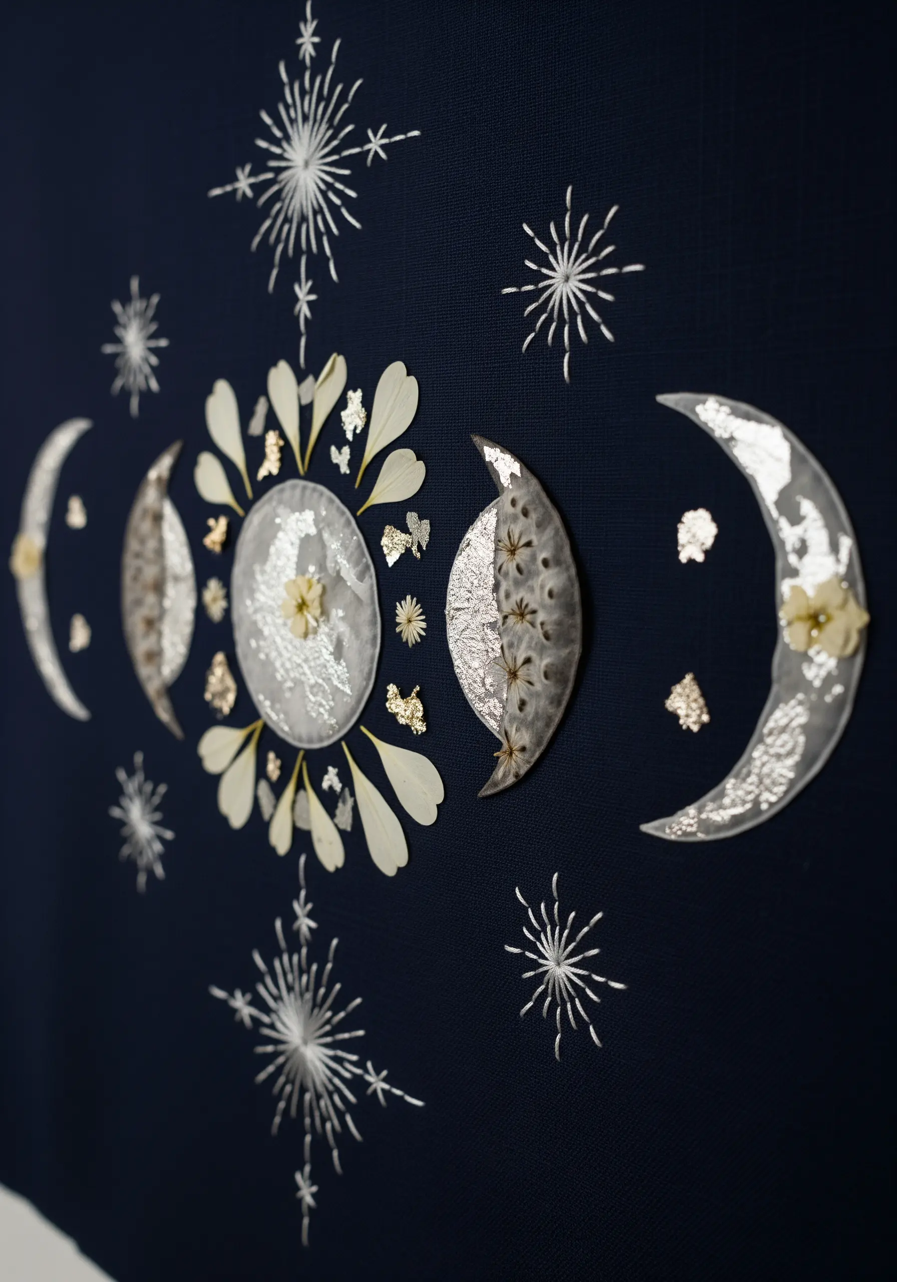 Moon phases created with white petals and silver leaf against a navy blue background.