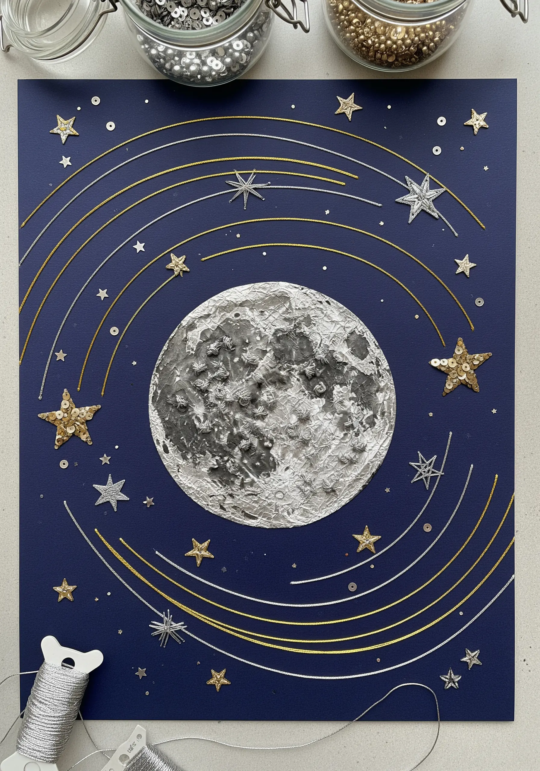 A celestial collage with a textured moon, metallic threads, and sequin stars.