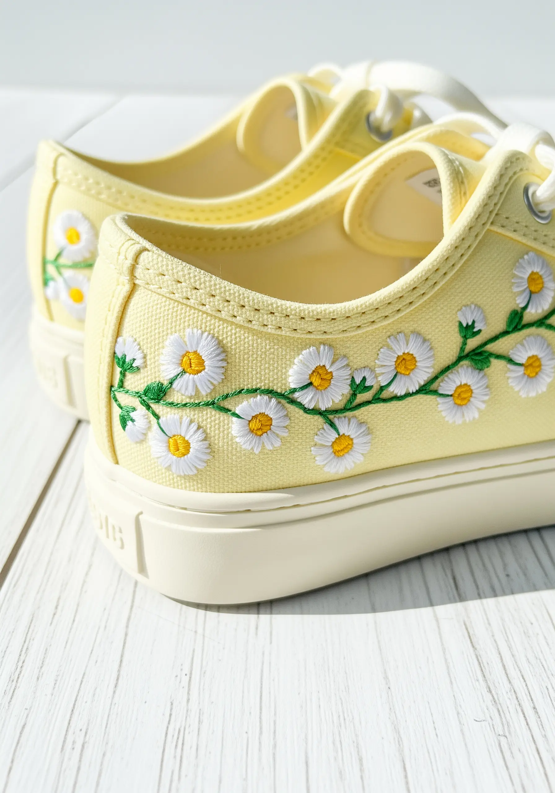 A cheerful chain of white and yellow daisies embroidered on pale yellow sneakers.