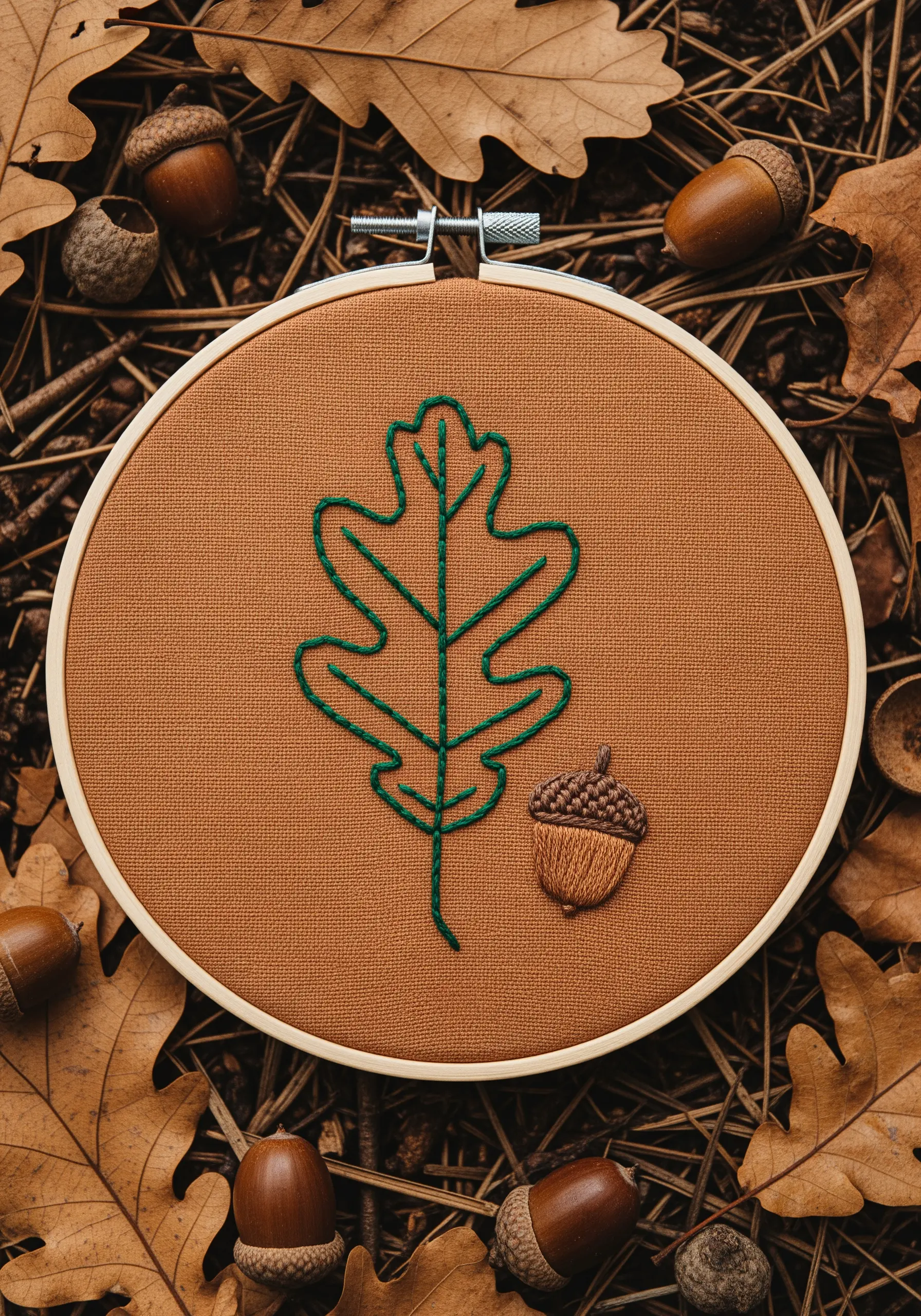 An outline of an oak leaf and a filled-in acorn embroidered on rust-colored fabric.