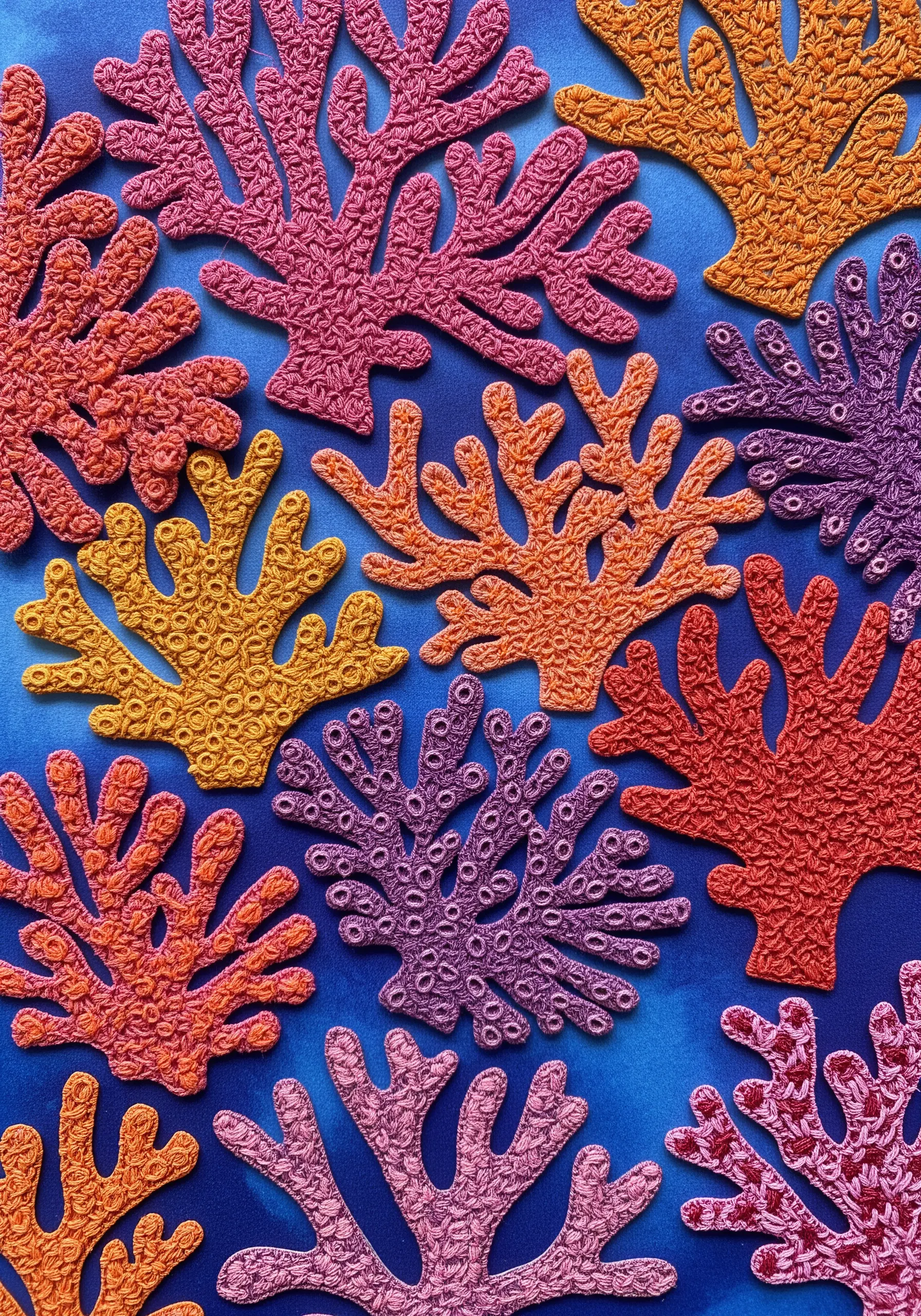 Densely embroidered coral shapes in various colors, cut out and arranged on a blue background.
